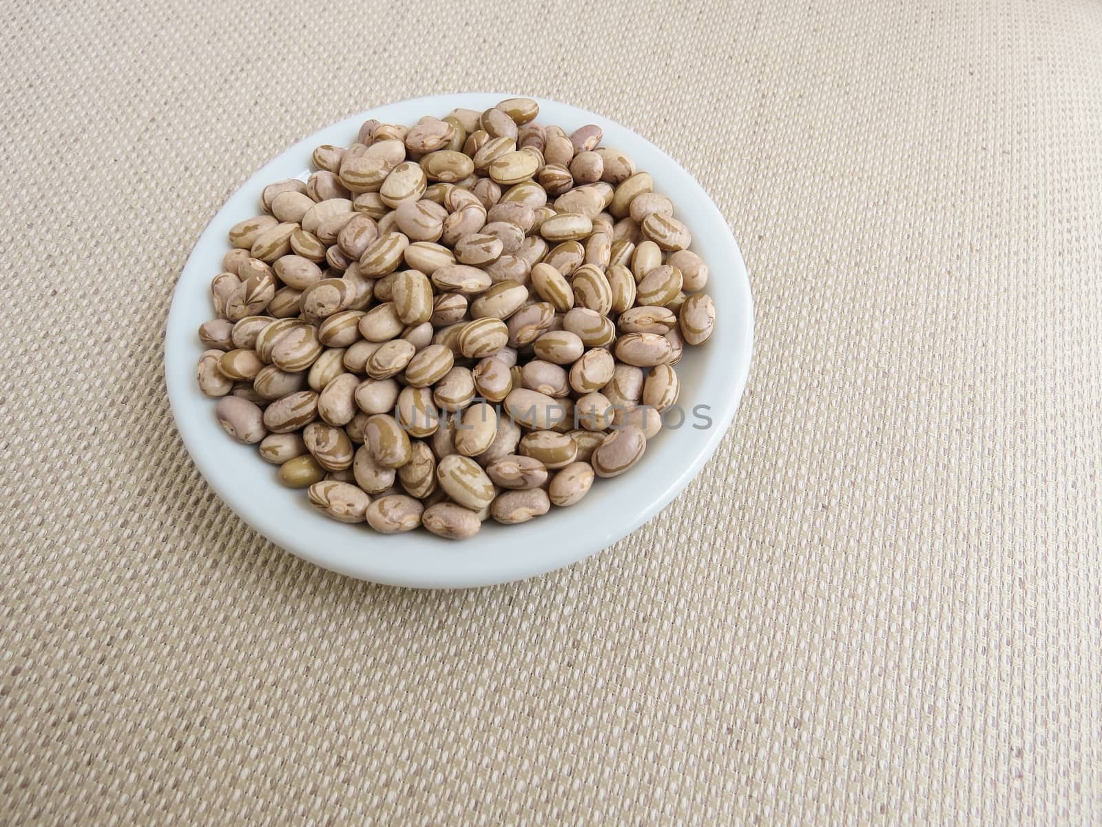 White plate with handful of raw carioca beans on a light cloth towel.
