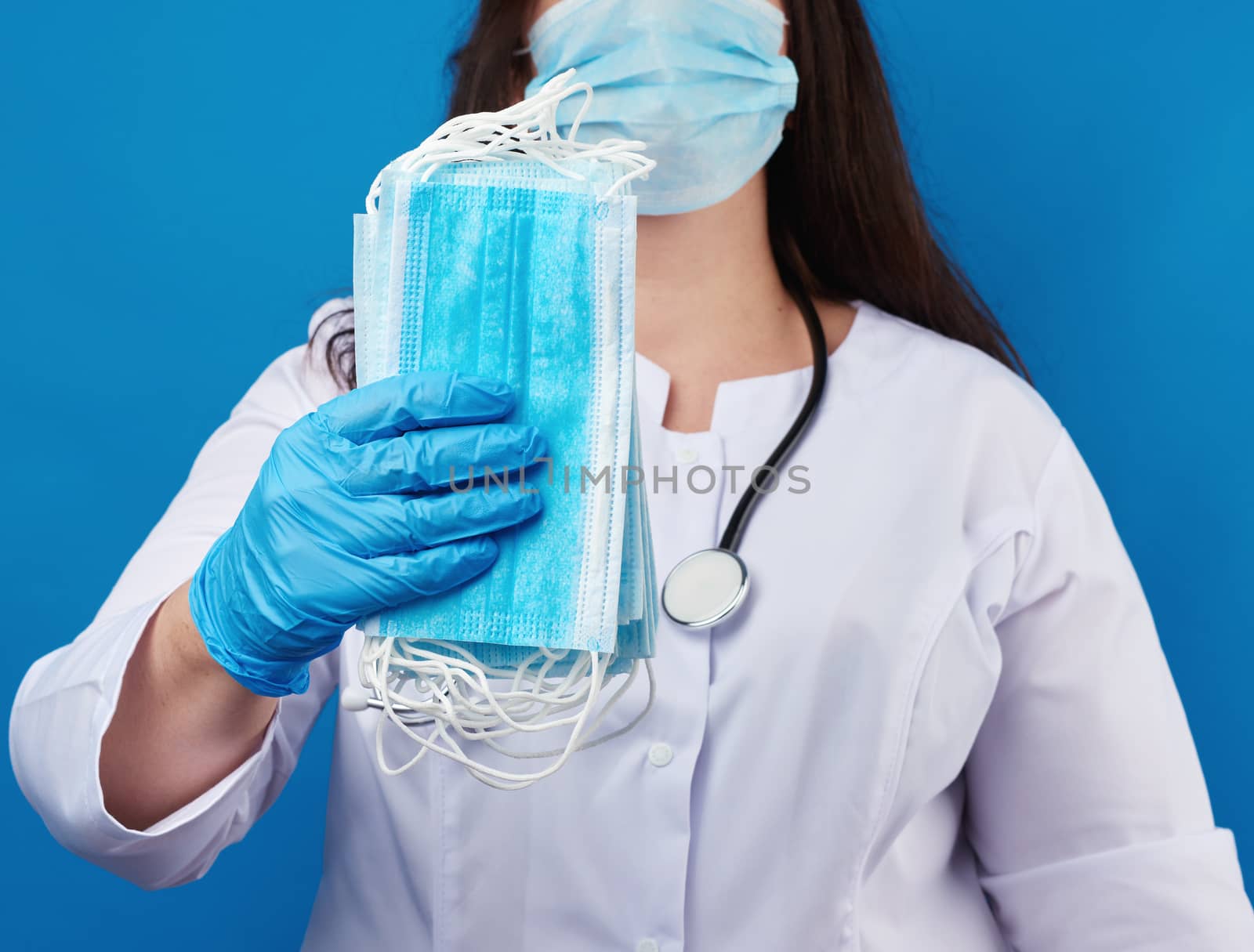 doctor in a white coat and mask holds a stack of protective disp by ndanko
