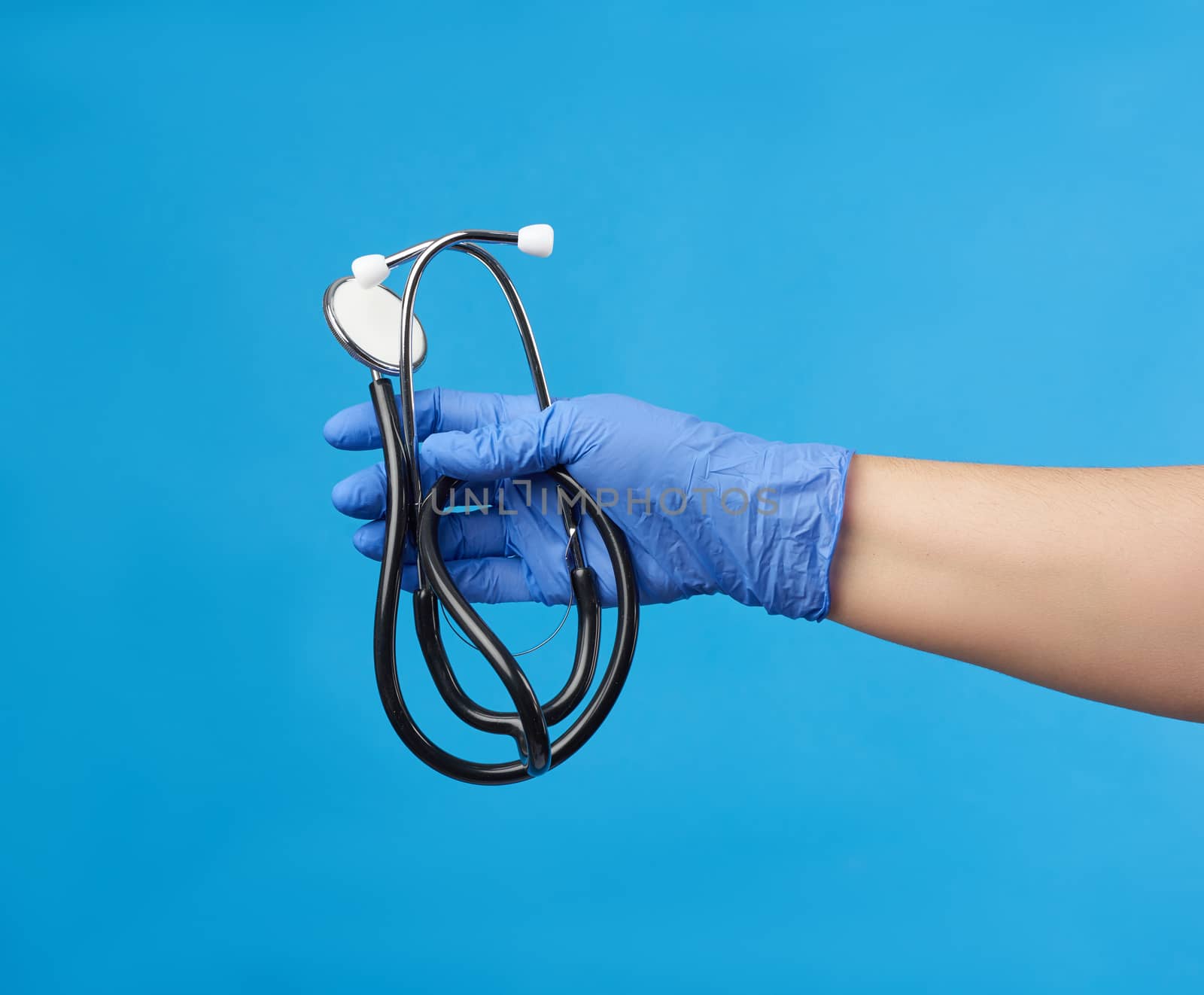 doctor in a white medical coat holds a black stethoscope on a blue background, close up