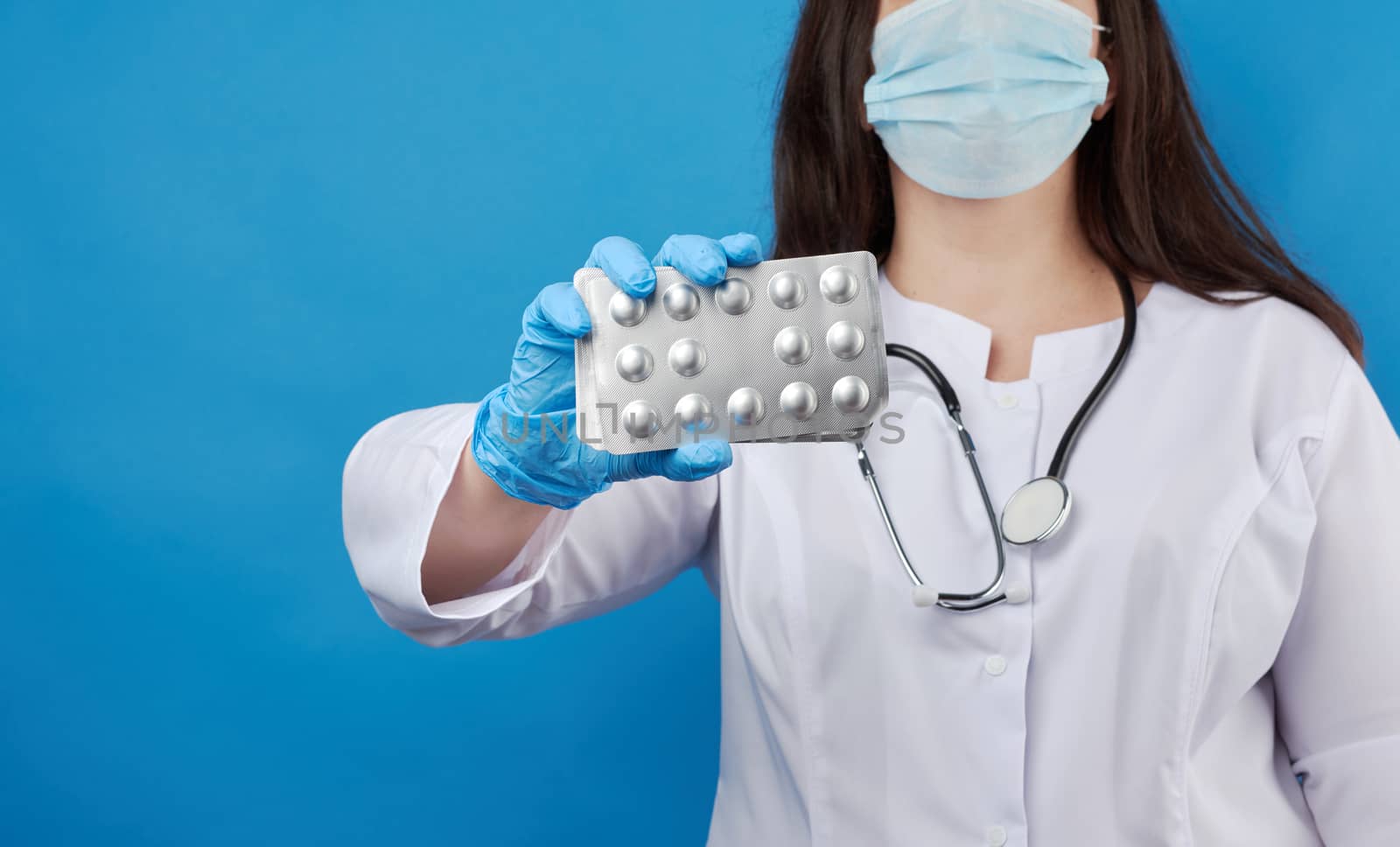 medic woman in white coat and blue latex gloves holds a pack of pills in a blister pack on a blue background