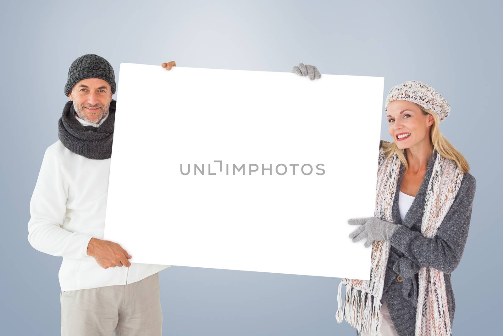 Smiling couple in winter fashion holding poster against grey vignette