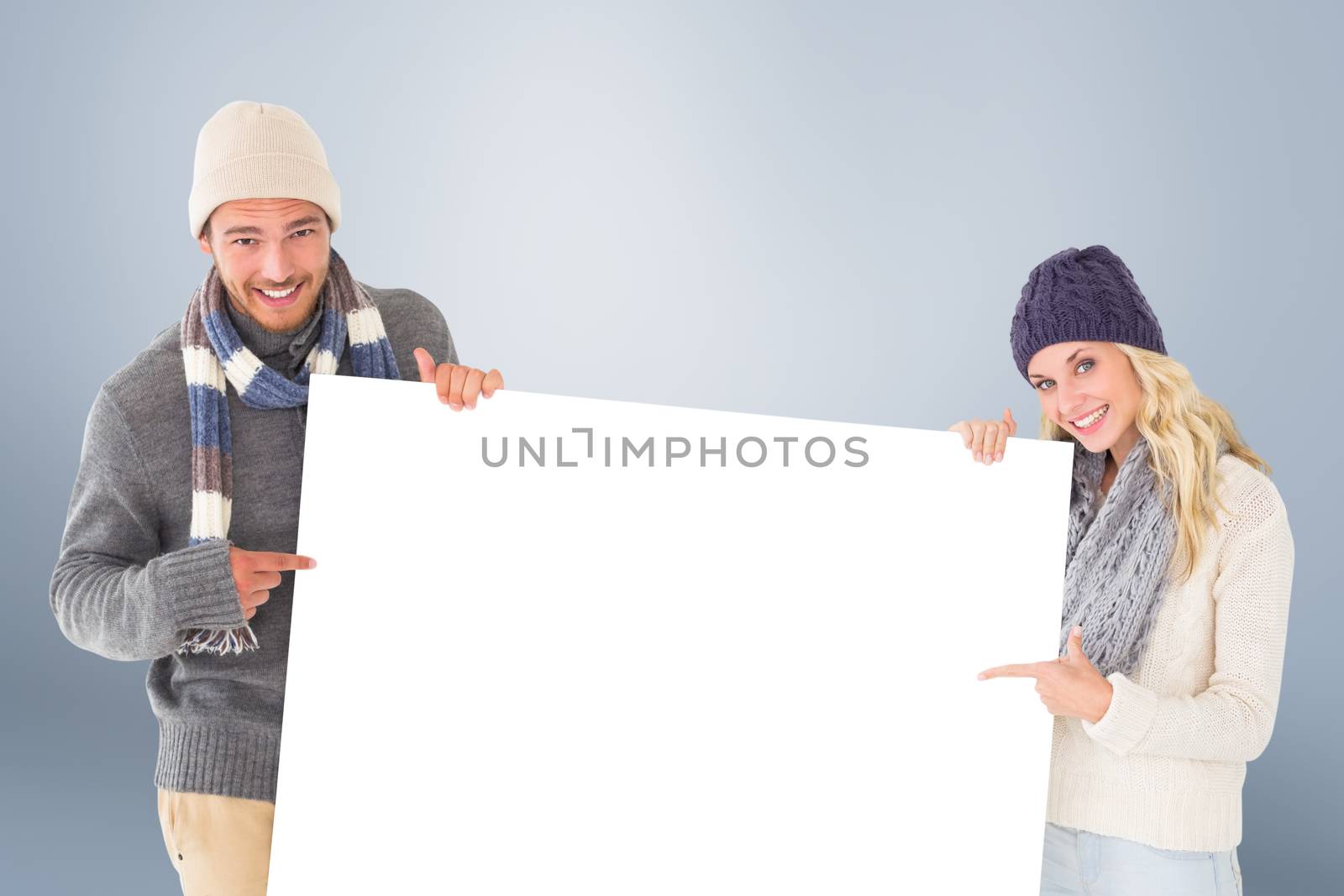 Attractive couple in winter fashion showing poster against grey vignette