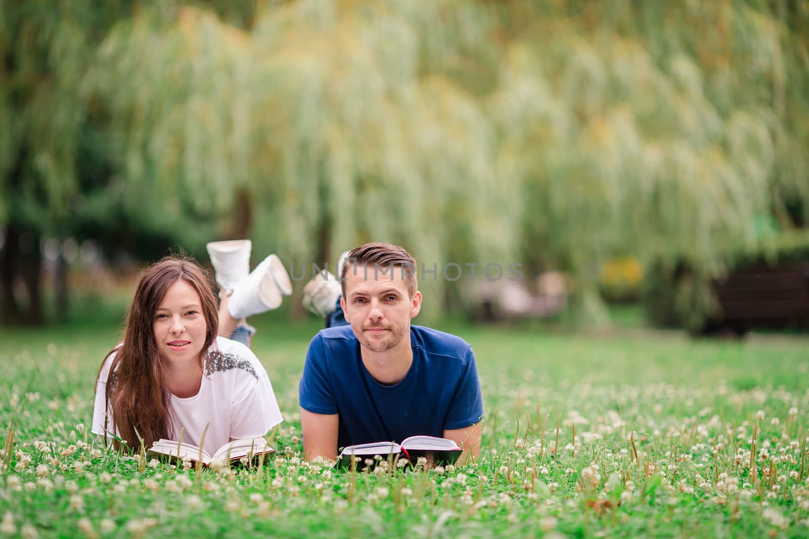 Relaxed young couple reading books while lying on grass by travnikovstudio