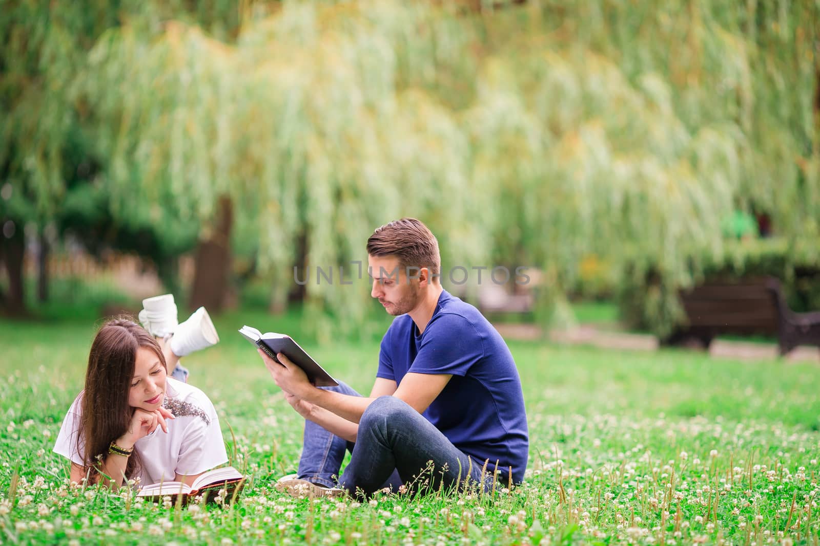 Relaxed young couple reading books while lying on grass by travnikovstudio