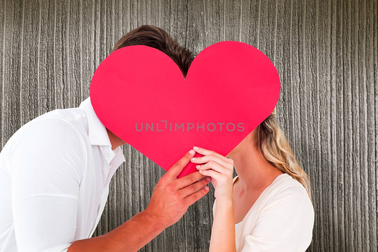 Attractive young couple kissing behind large heart against wooden planks