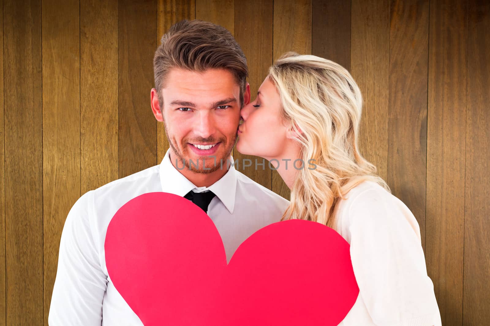 Attractive young couple holding red heart against wooden surface with planks