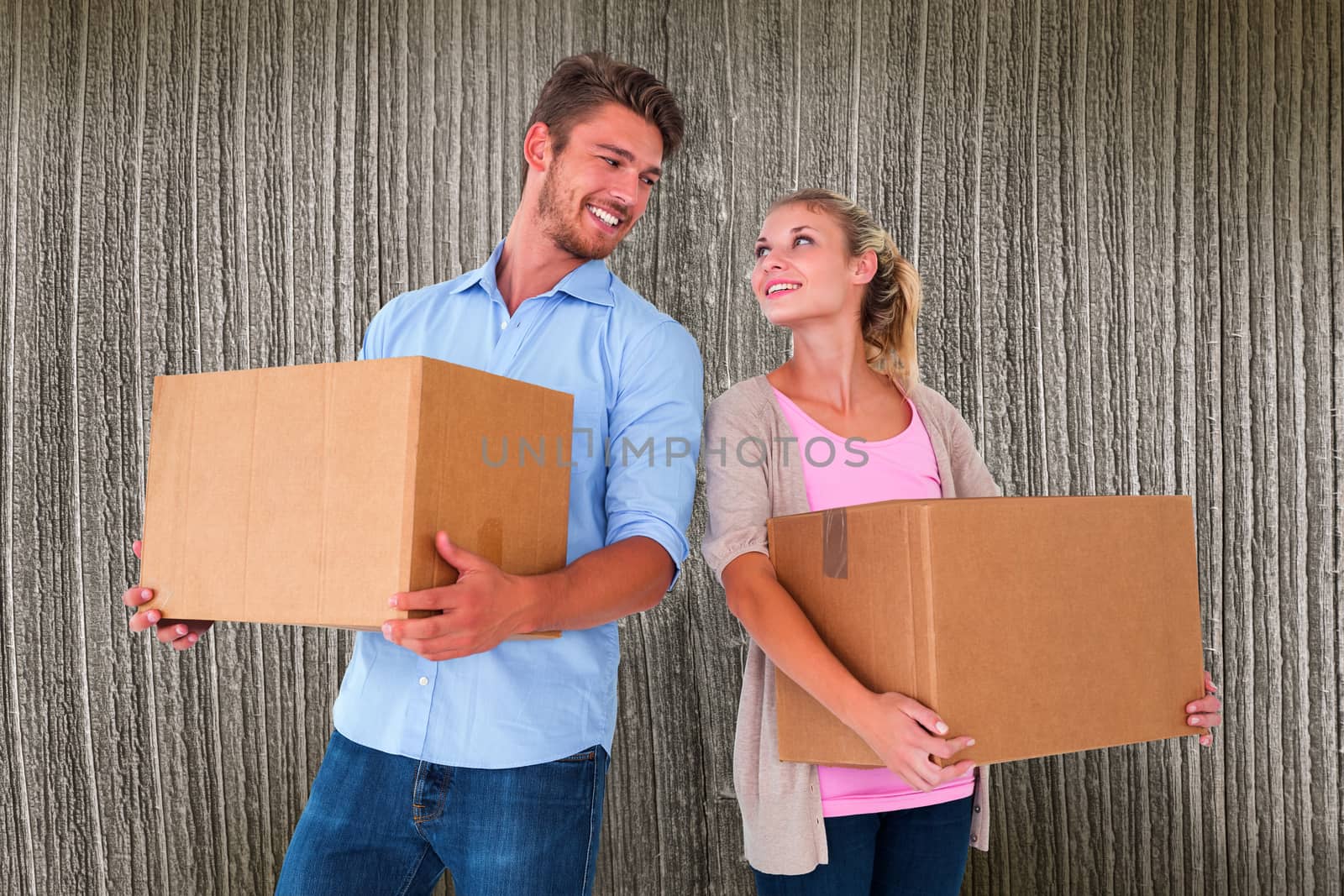 Attractive young couple carrying moving boxes against wooden planks