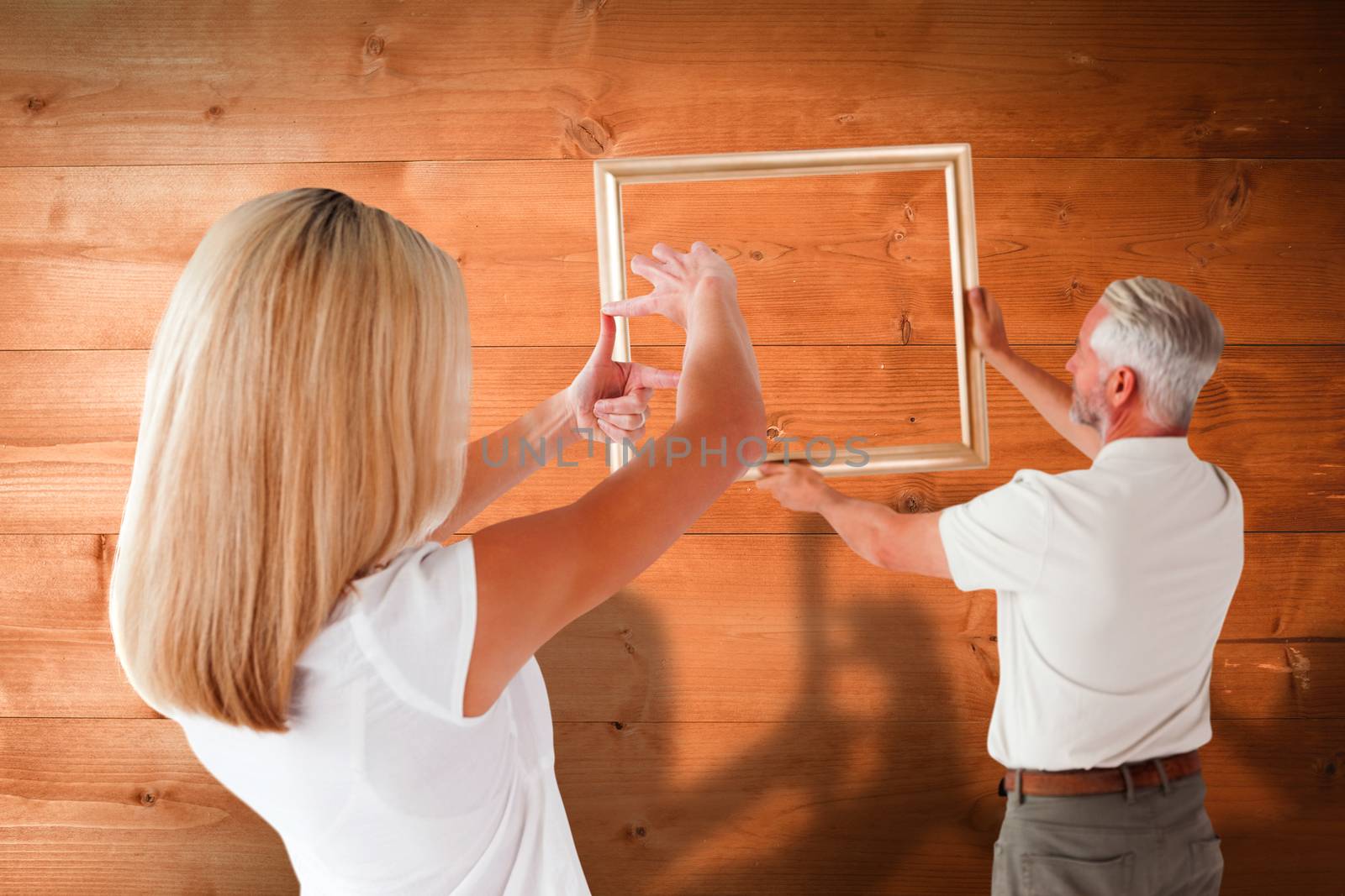 Couple hanging a frame together against overhead of wooden planks