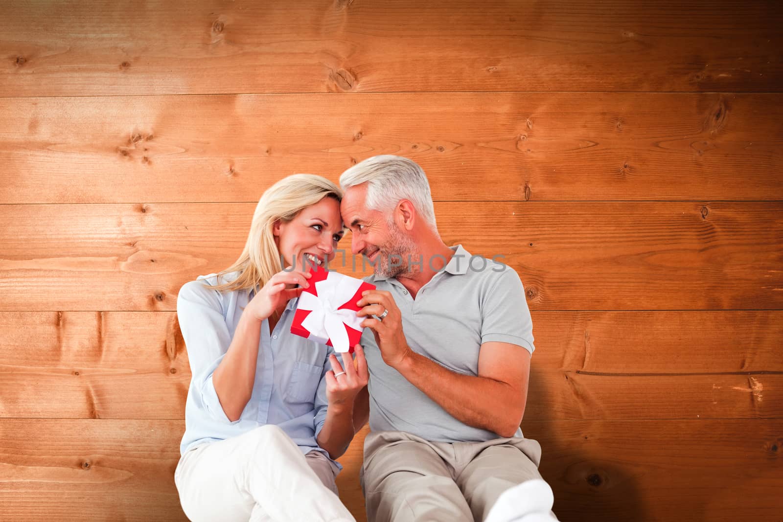 Happy couple sitting and holding present against overhead of wooden planks