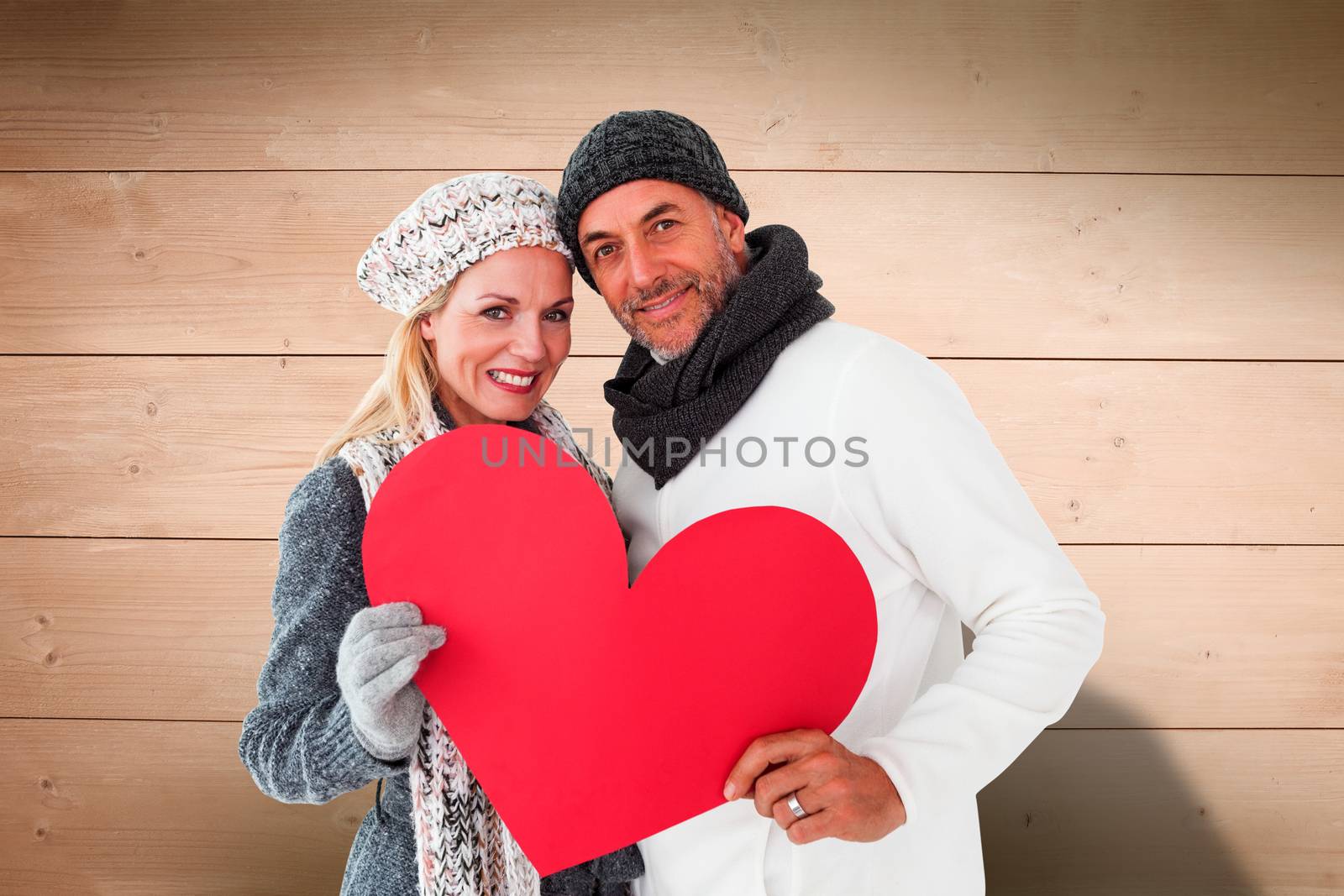 Smiling couple in winter fashion posing with heart shape against overhead of wooden planks