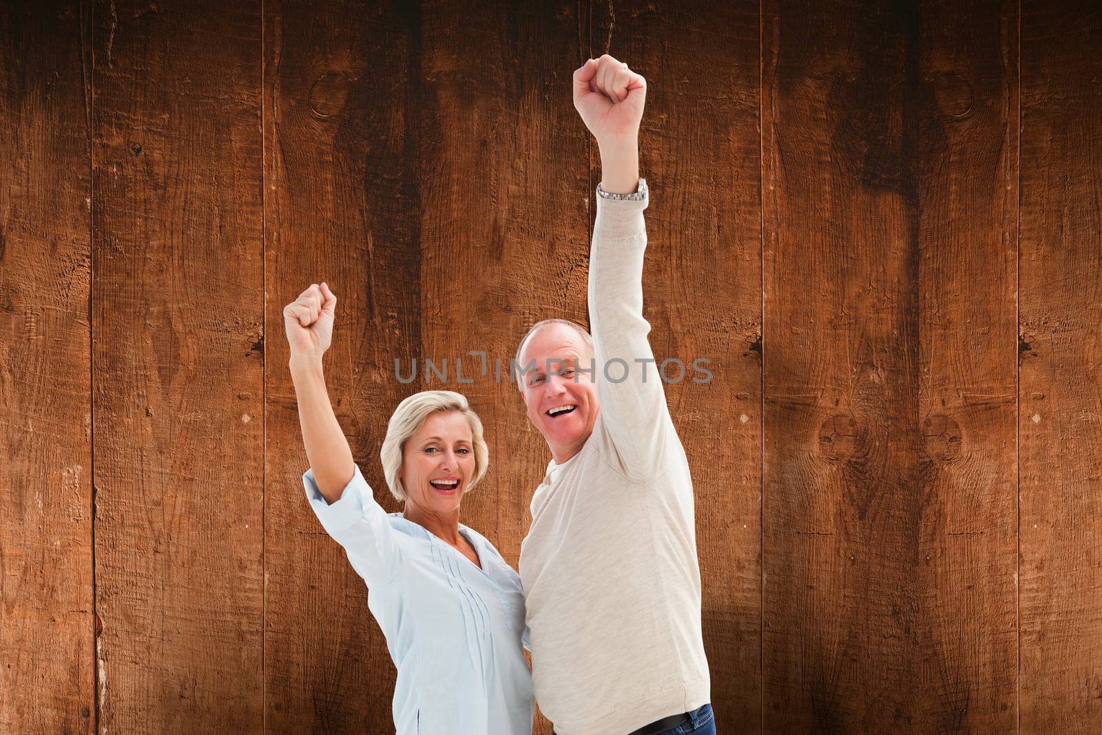 Happy mature couple cheering at camera against weathered oak floor boards background