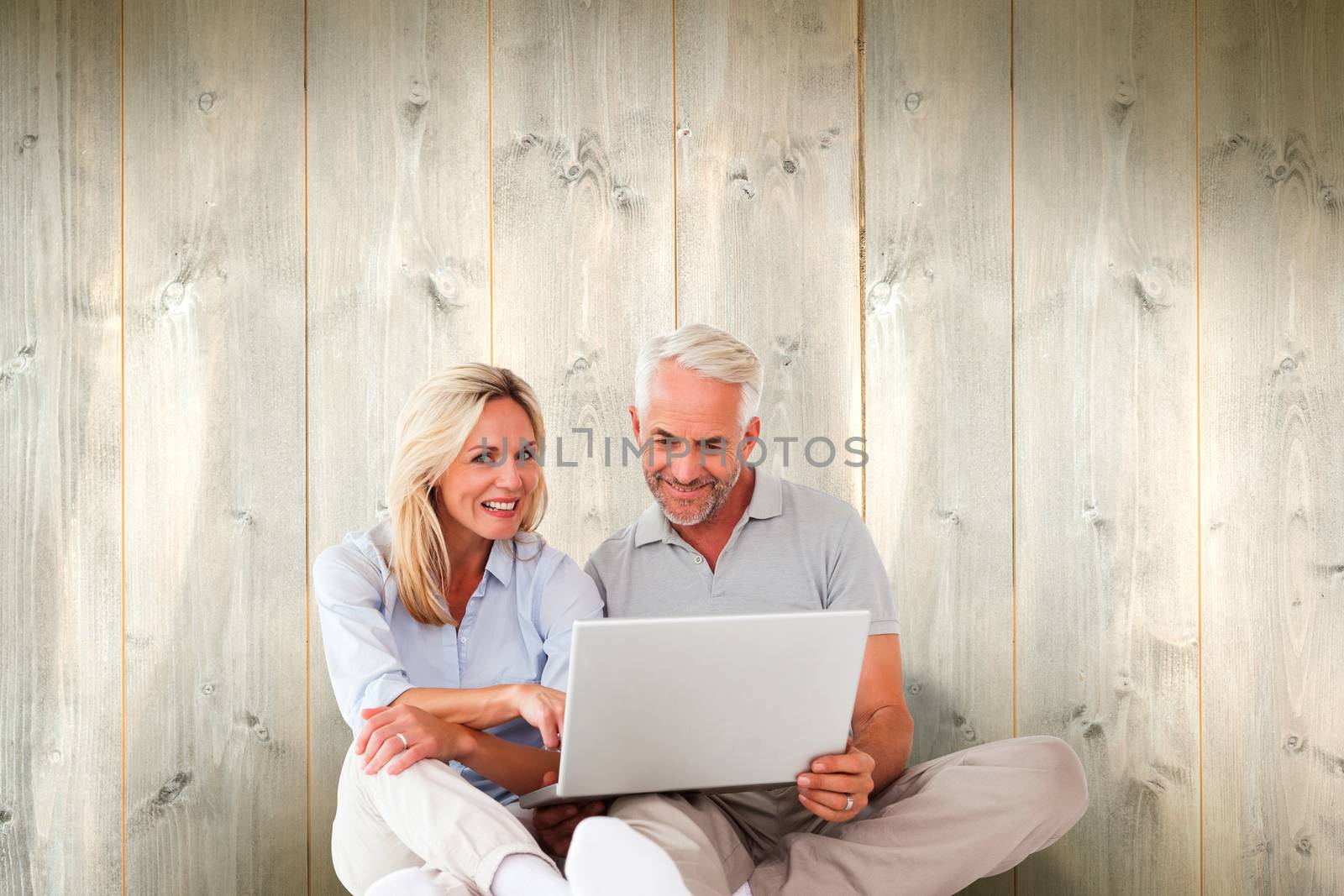 Happy couple sitting and using laptop against pale wooden planks