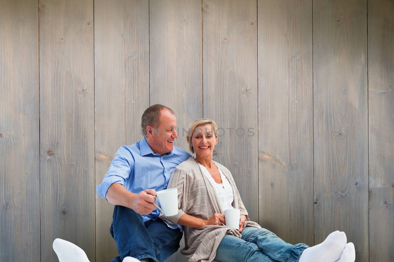 Happy mature couple having coffee against pale grey wooden planks
