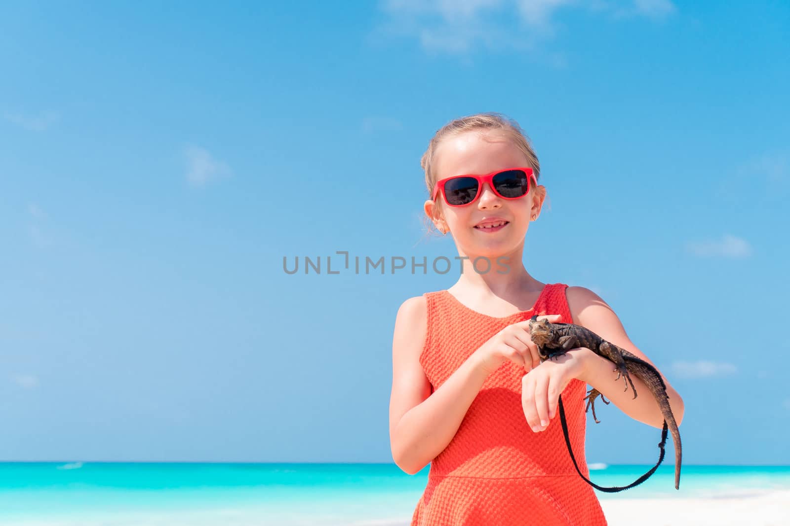 Adorable little girl happily holds a wild tropical lizard on white tropical beach by travnikovstudio