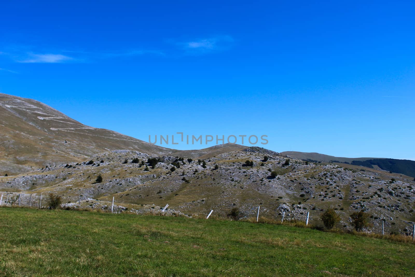 A meadow with a downed fence at the end of the meadow. In the background, mountain desolation, with little vegetation. On the way to the mountain Bjelasnica, Bosnia and Herzegovina.