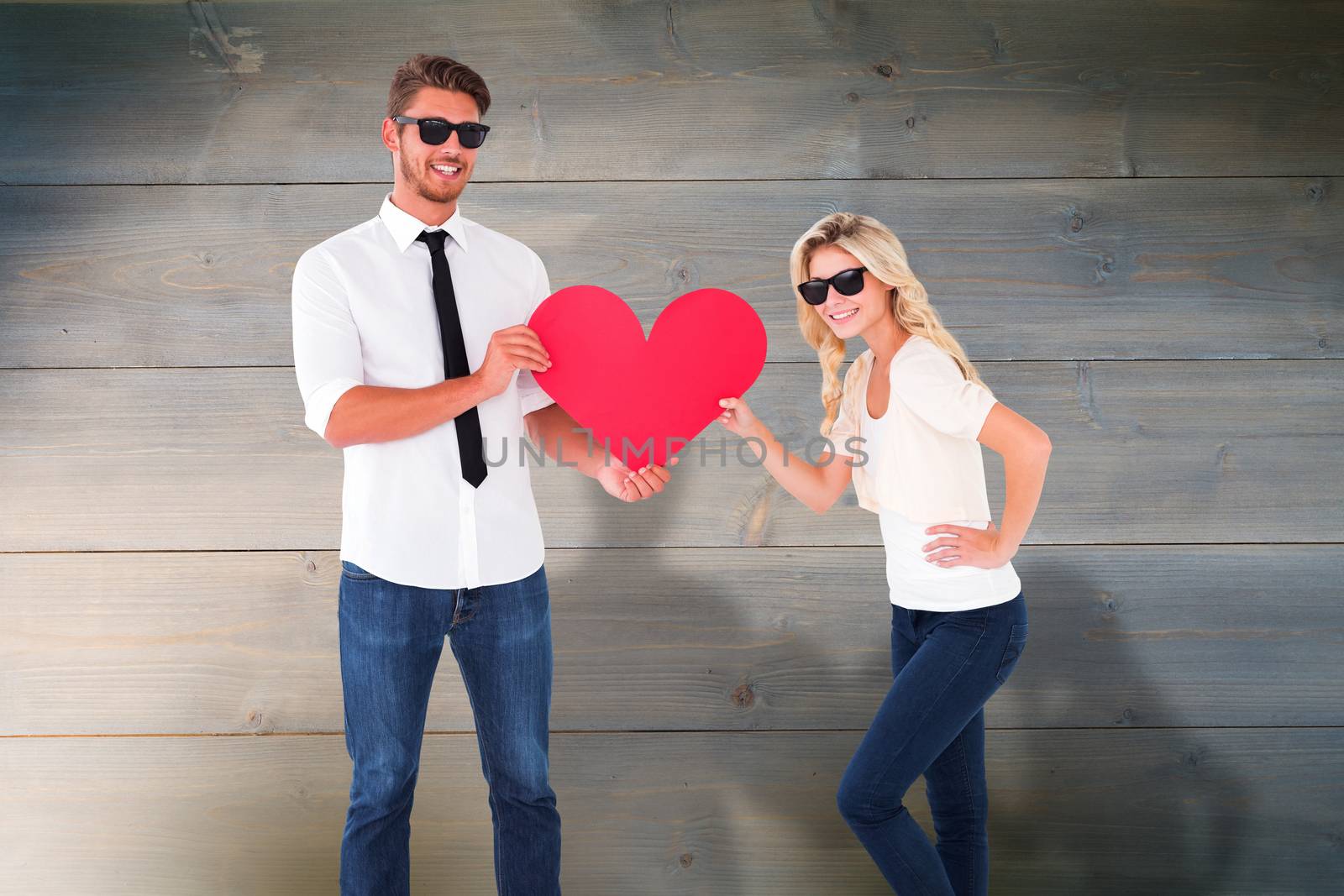 Cool young couple holding red heart against bleached wooden planks background