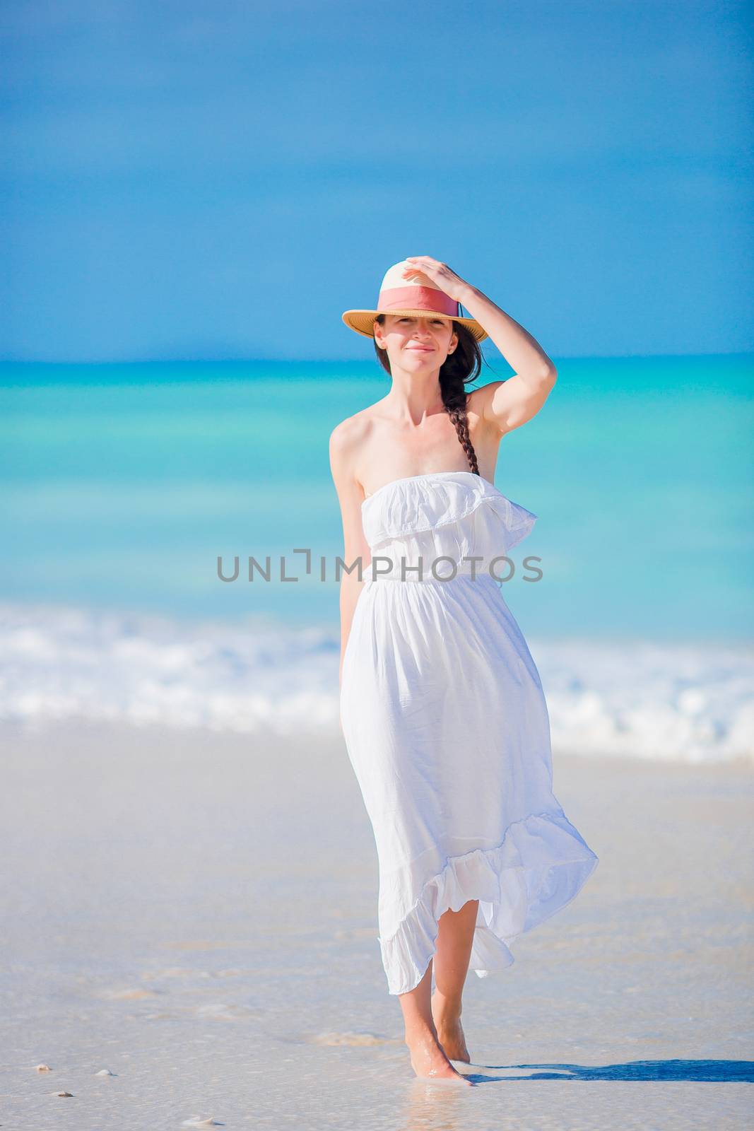 Young beautiful woman on white sand tropical beach. Caucasian girl with hat background the sea by travnikovstudio