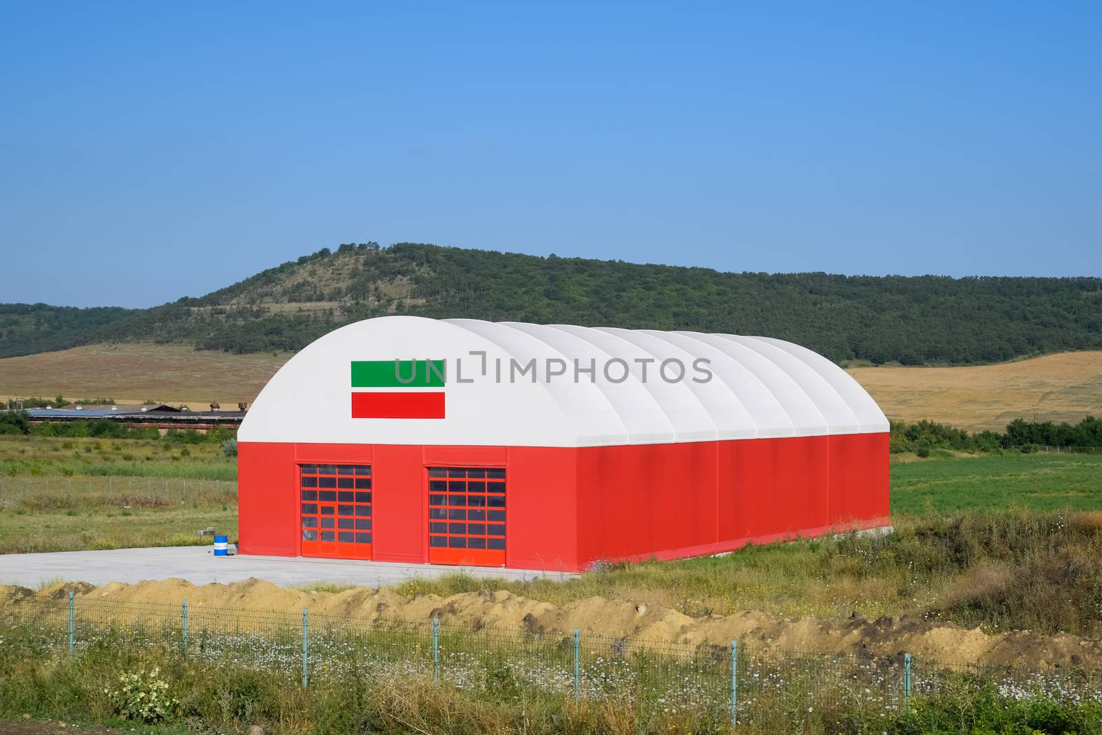 The hangar is white and red. An hangar in a field.