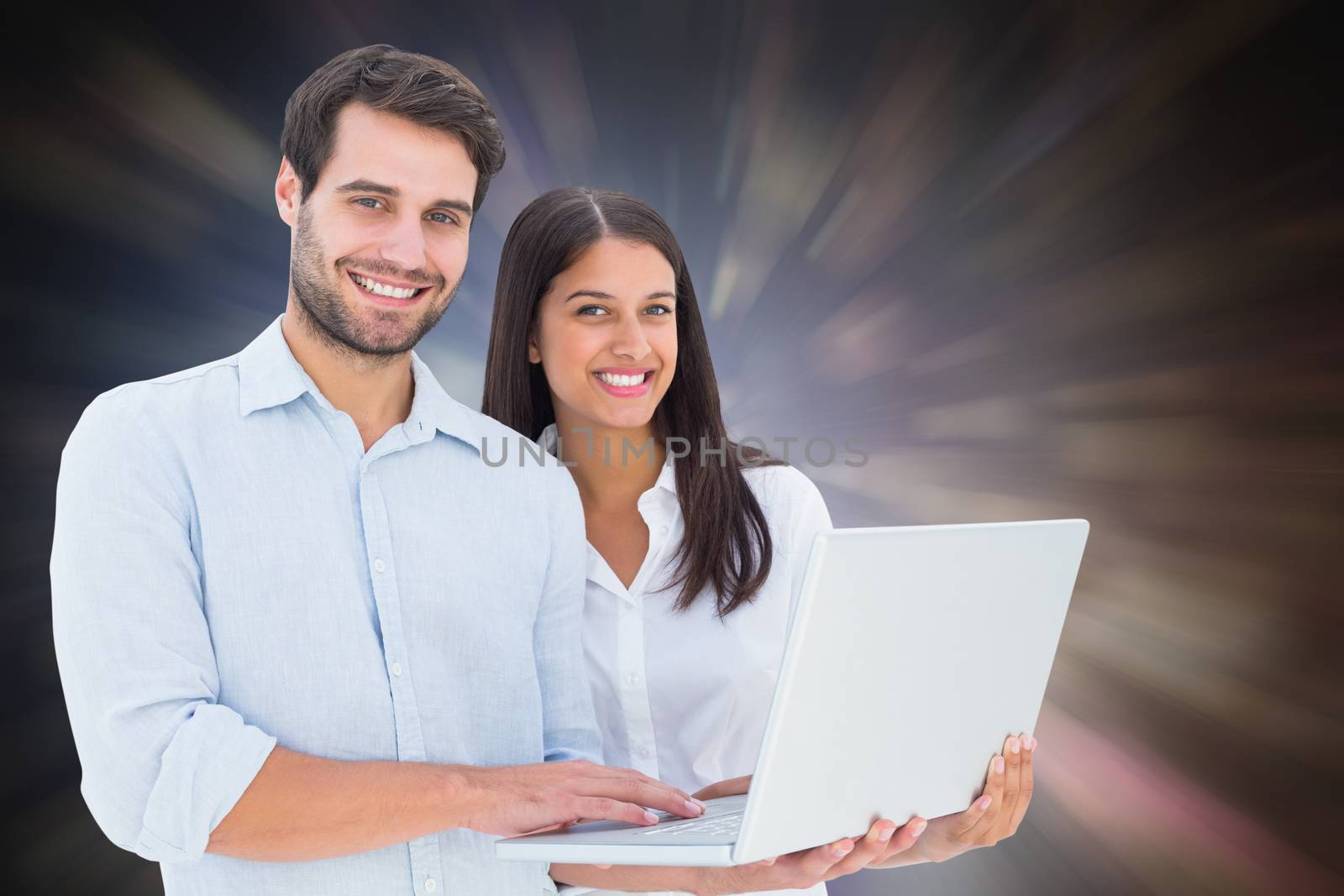 Attractive young couple holding their laptop against dark abstract light spot design