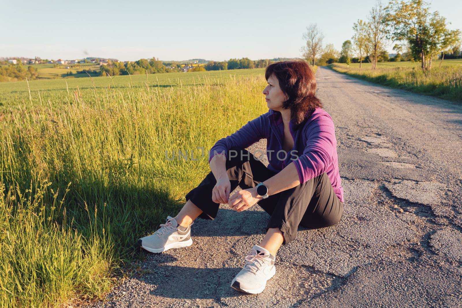 happy european woman resting during running workout on asphalt road on sunset. Attractive and healthy middle age women in countryside.