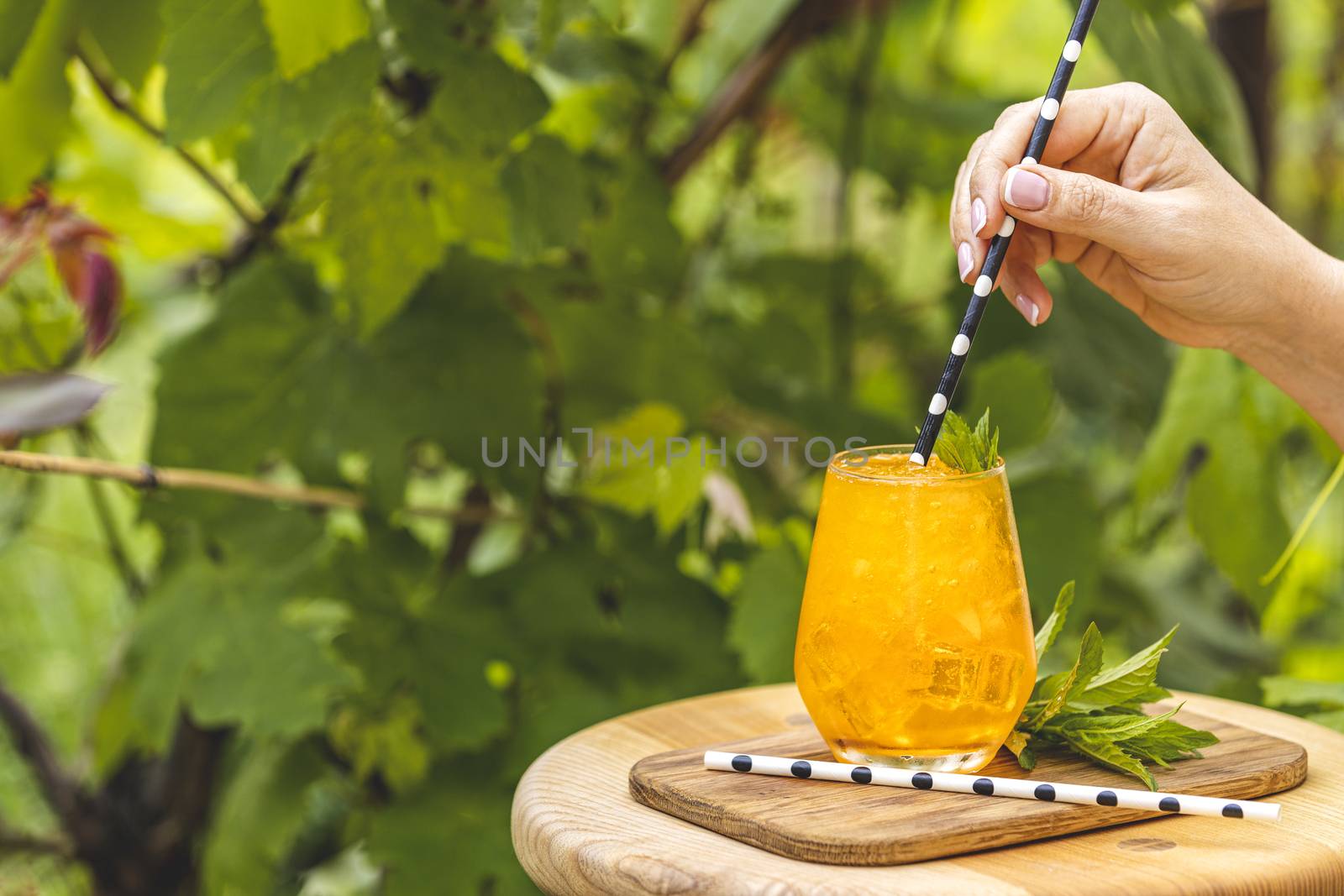 Woman hand holding drinking straw over orange drink with ice on  by ArtSvitlyna