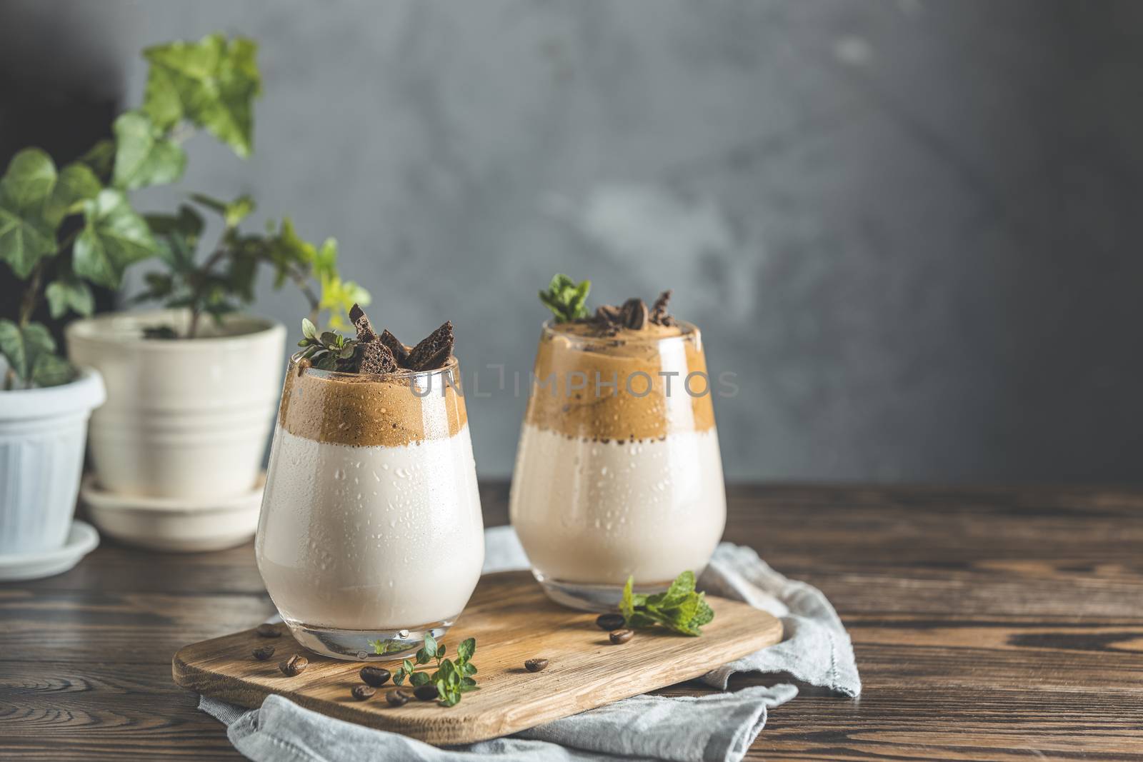 Two glasses with Dalgona frothy coffee trend korean drink latte espresso with coffee foam, decorated by thyme and dark chocolate. Dark wooden table surface