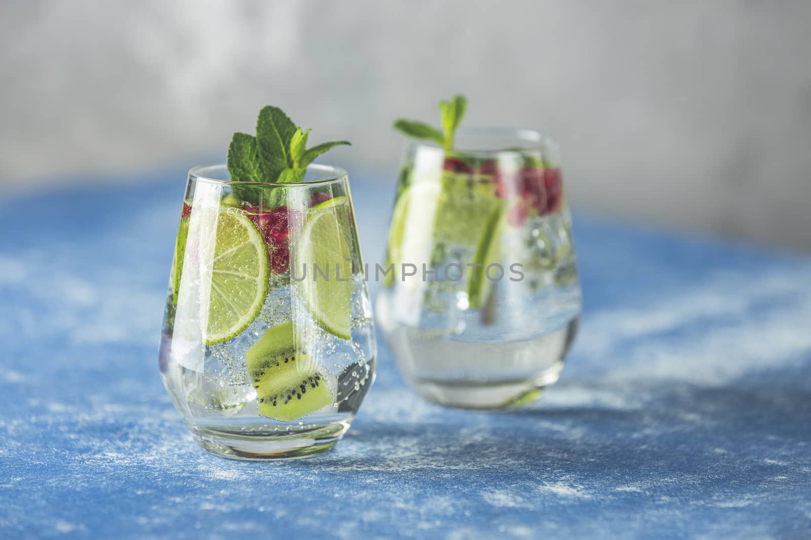 Detox water or martini tonic cocktail with kiwi, lime and ice, decoration pomegranate and mint. Summer fresh lime soda cocktail, selective focus	