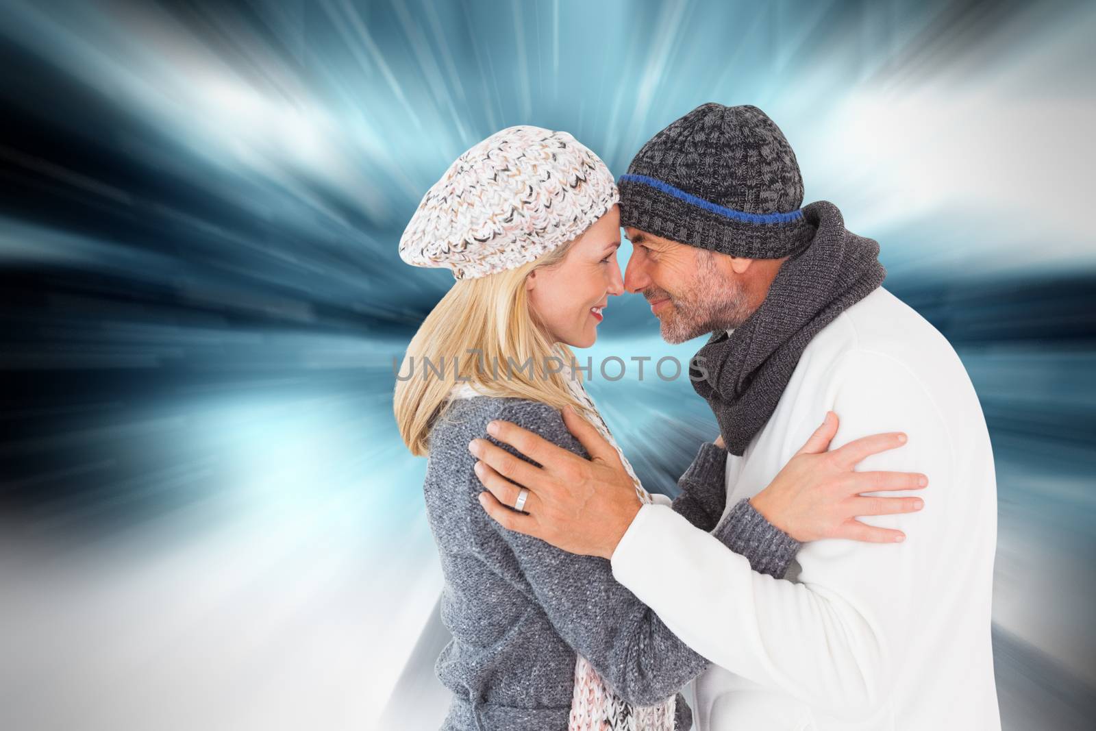 Happy couple in winter fashion embracing against large rock overlooking snowy sky