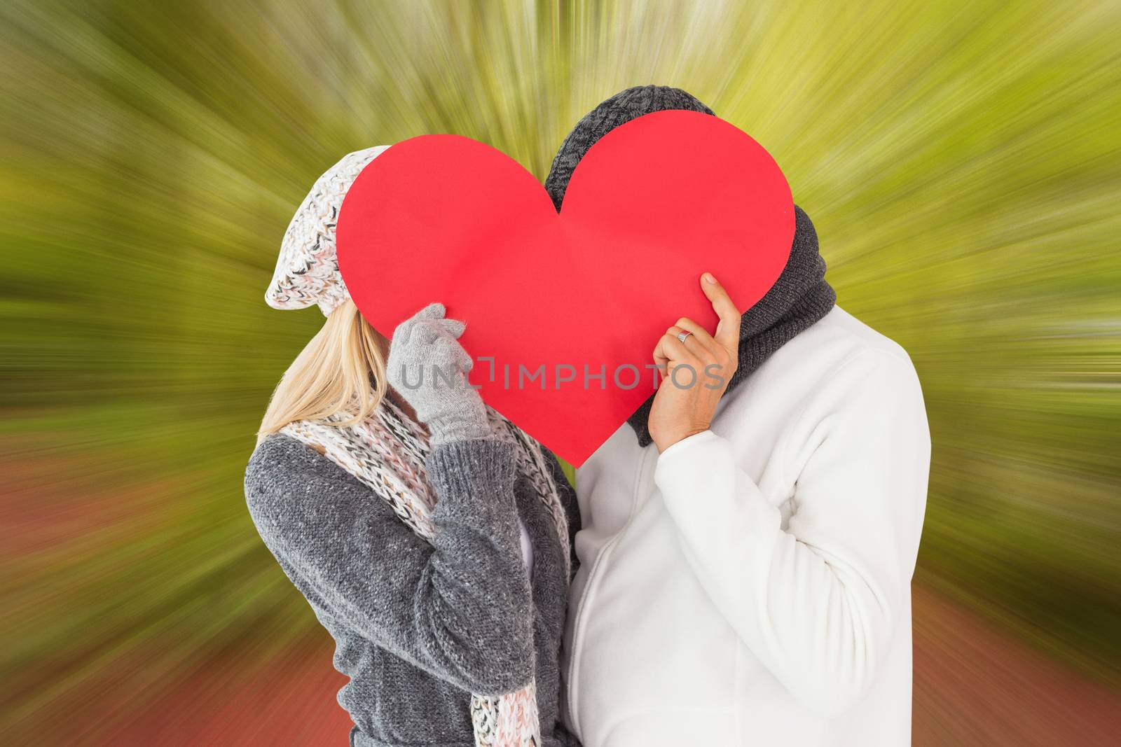 Couple in winter fashion posing with heart shape against peaceful autumn scene in forest