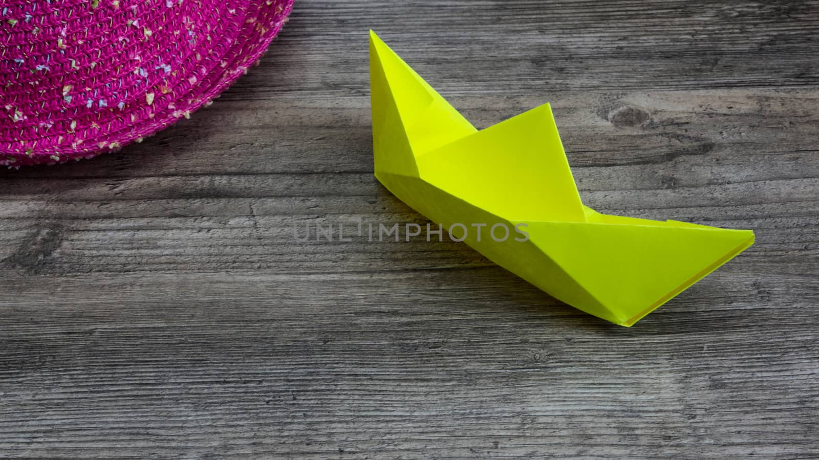 Origami, yellow ship of paper and pink hat on wooden table, hobby