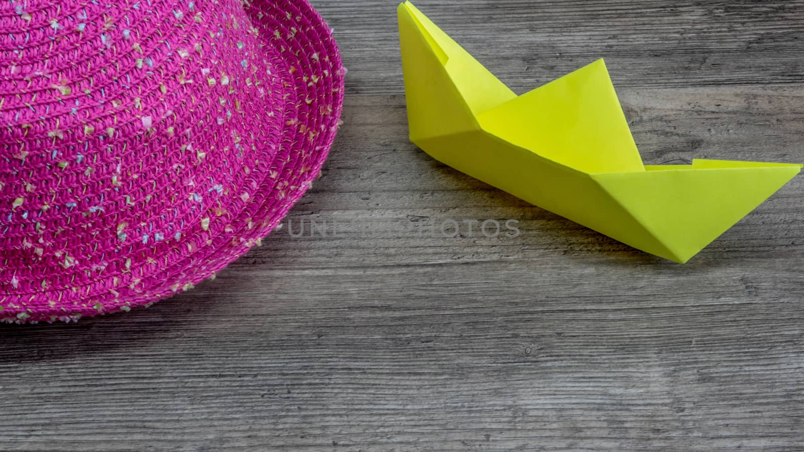 Origami, yellow ship of paper and pink hat on wooden table, hobby