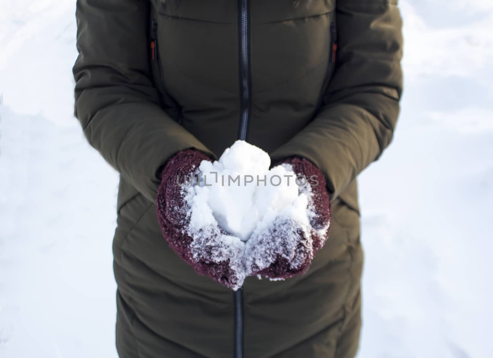 One person holds a snowball in winter in the Park, walk, fun, sports and leisure, green jacket, Burgundy mittens