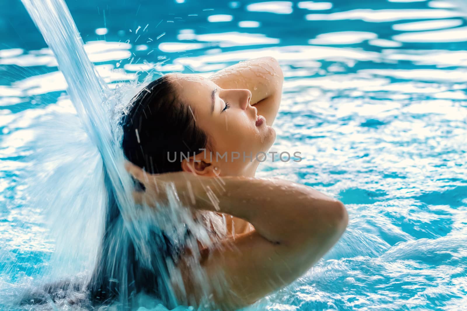 Close up portrait of young girl with relaxed facial expression under high pressure shower in spa.Woman touching hair with eyes closed.