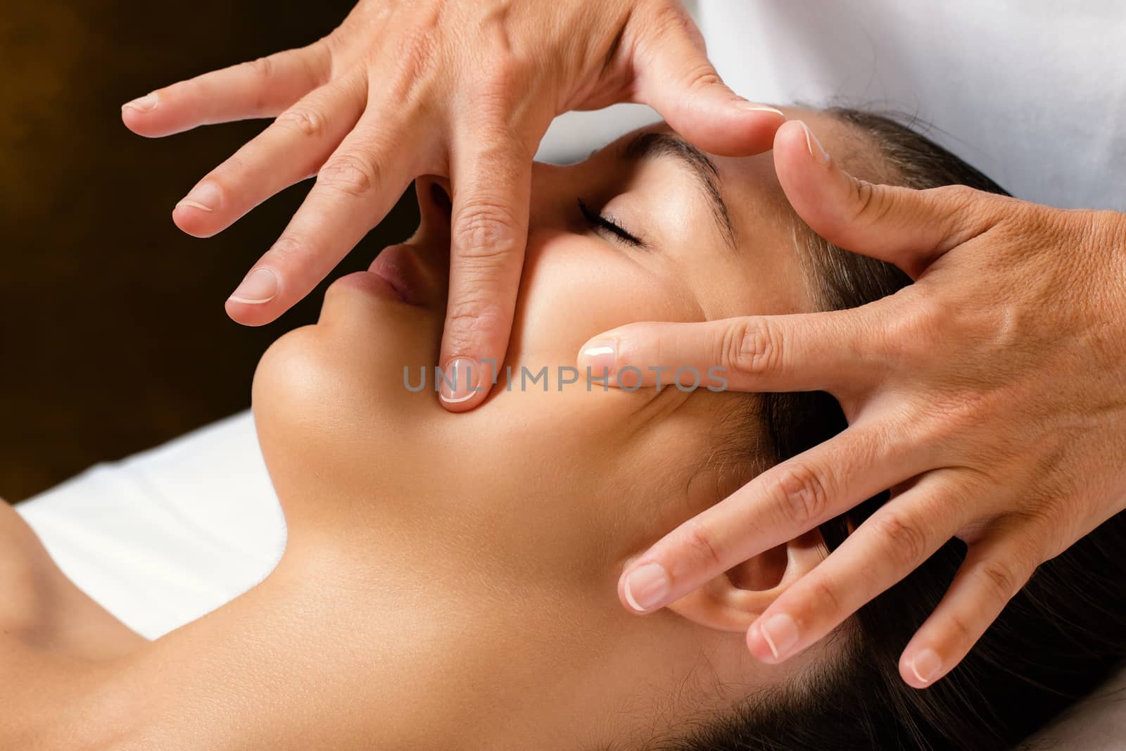 Close up portrait of woman at beauty treatment in spa.Therapist massaging and stretching female cheek for product penetration.