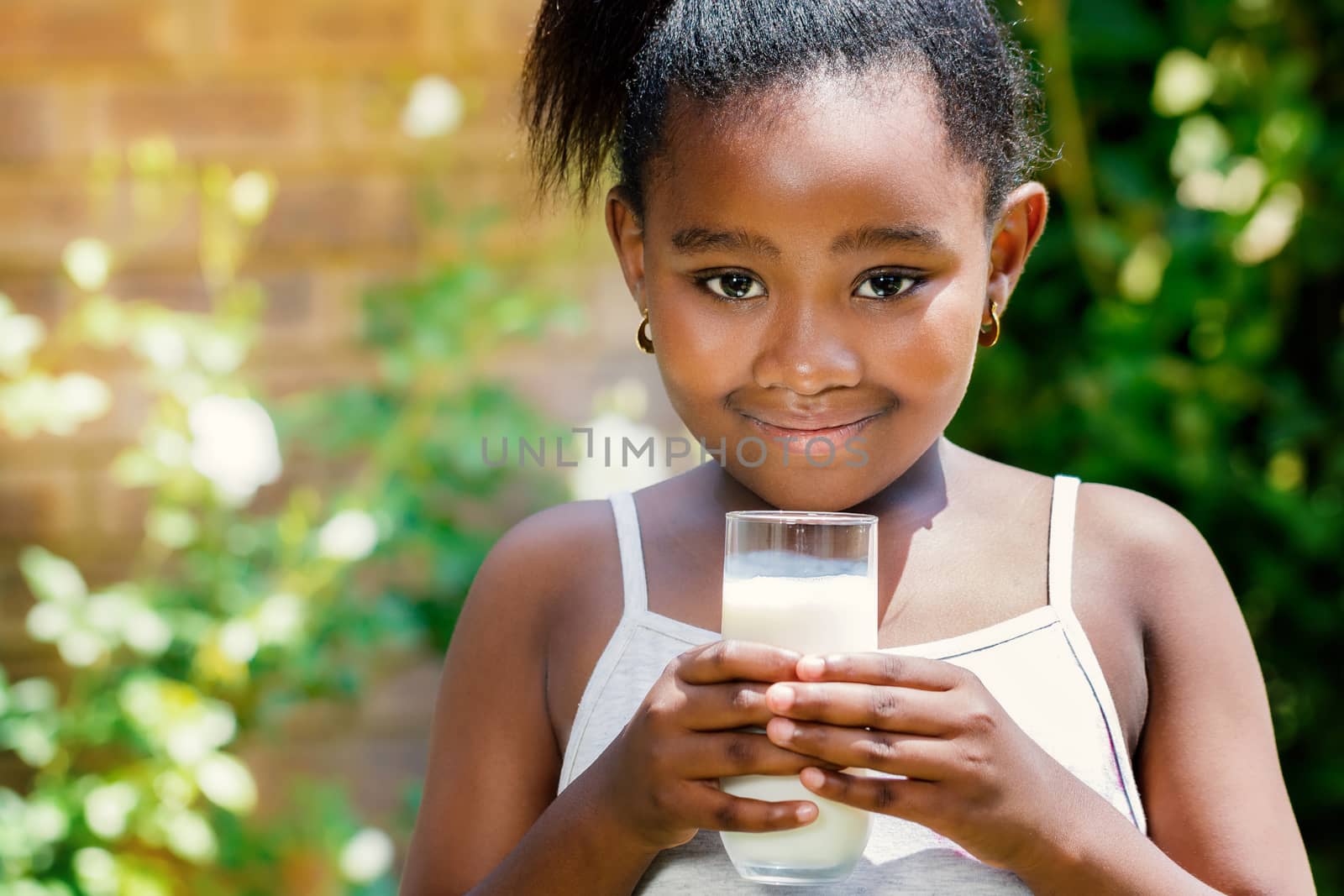 Close up portrait of cute little african girl holding glass with milk in garden.