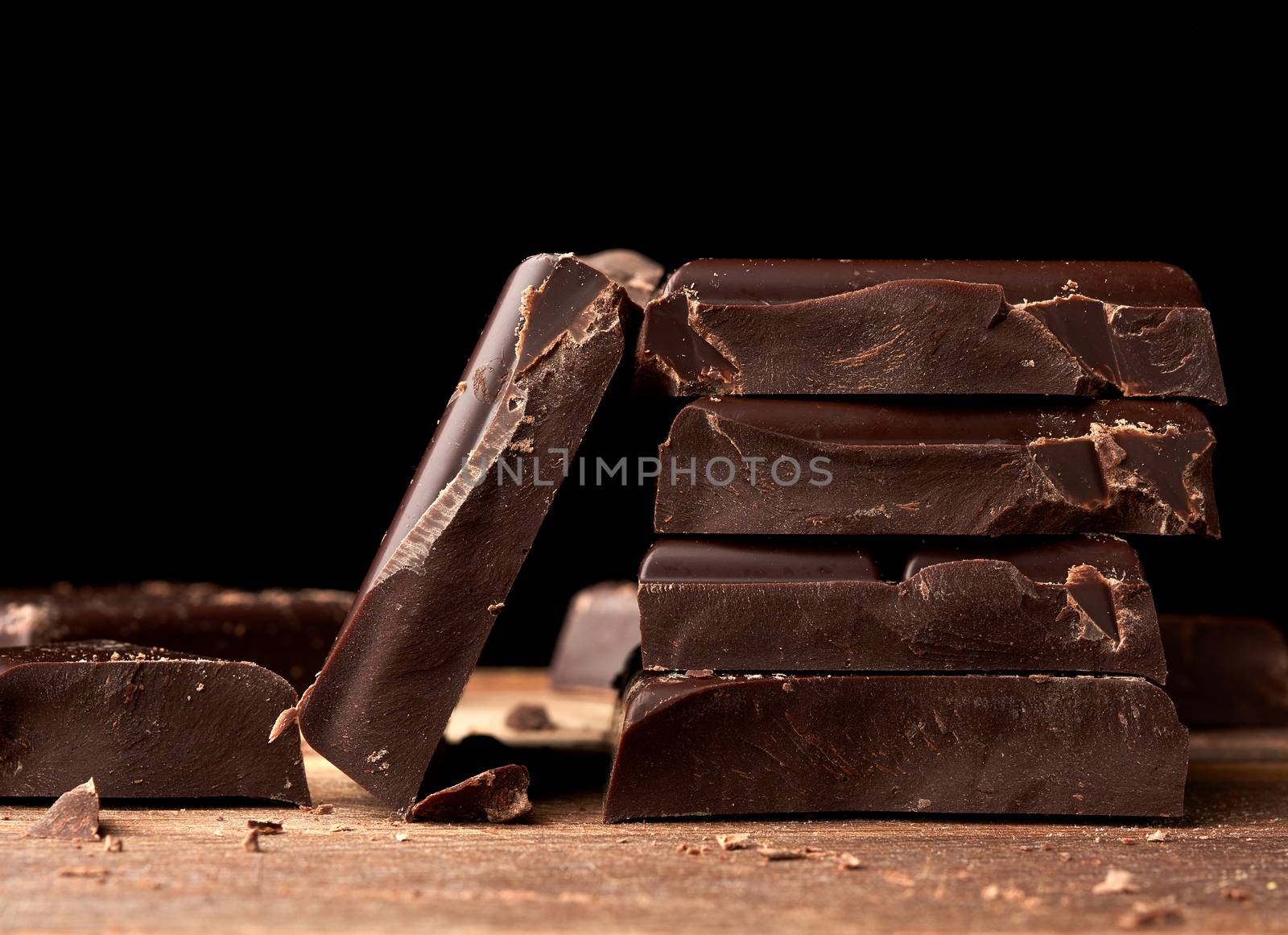 broken black chocolate on a wooden table, culinary sweet ingredi by ndanko