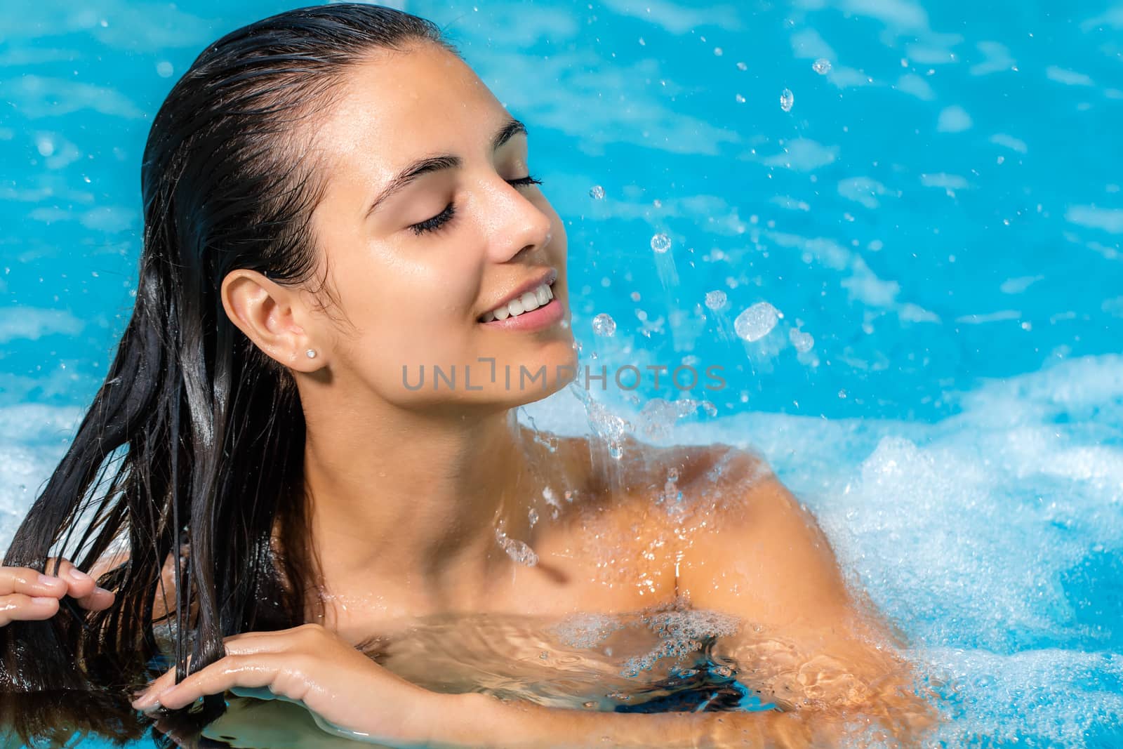 Close up portrait of attractive brunette relaxing in spa jacuzzi. Woman with relaxed face expression touching hair.