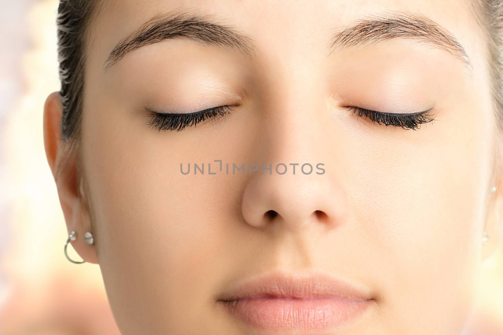 Extreme close up face shot of attractive young woman meditating with eyes closed against colorful bright background.
