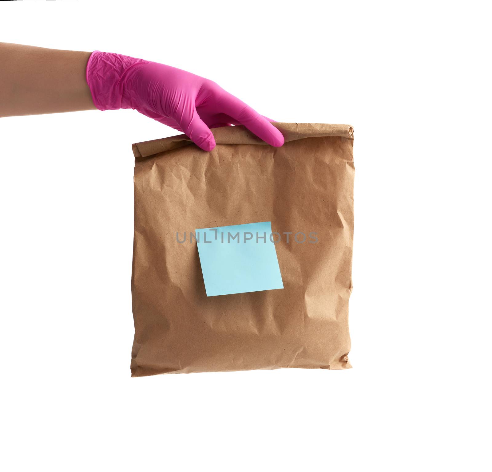 hand in pink latex glove holds a disposable bag of brown craft paper with a sticker on a white isolated background, concept of contactless delivery of food and orders from online stores, safe shopping