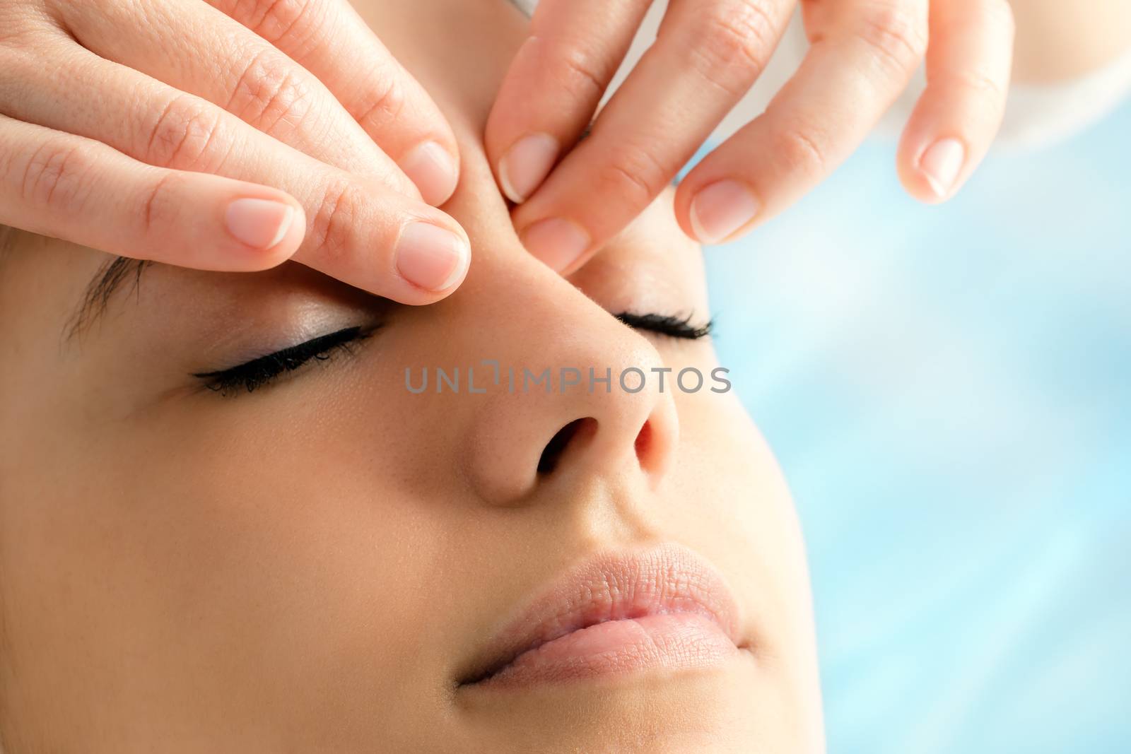 Extreme close up of therapist doing reiki on young woman.Fingers applying pressure between eyes.