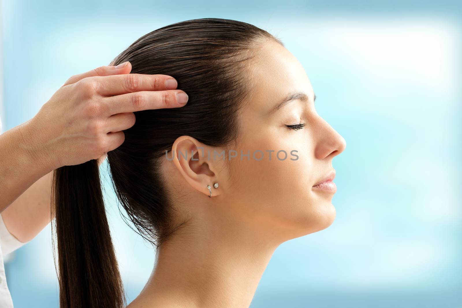 Close up portrait of woman at reiki session. Therapist touching side of head with hands.
