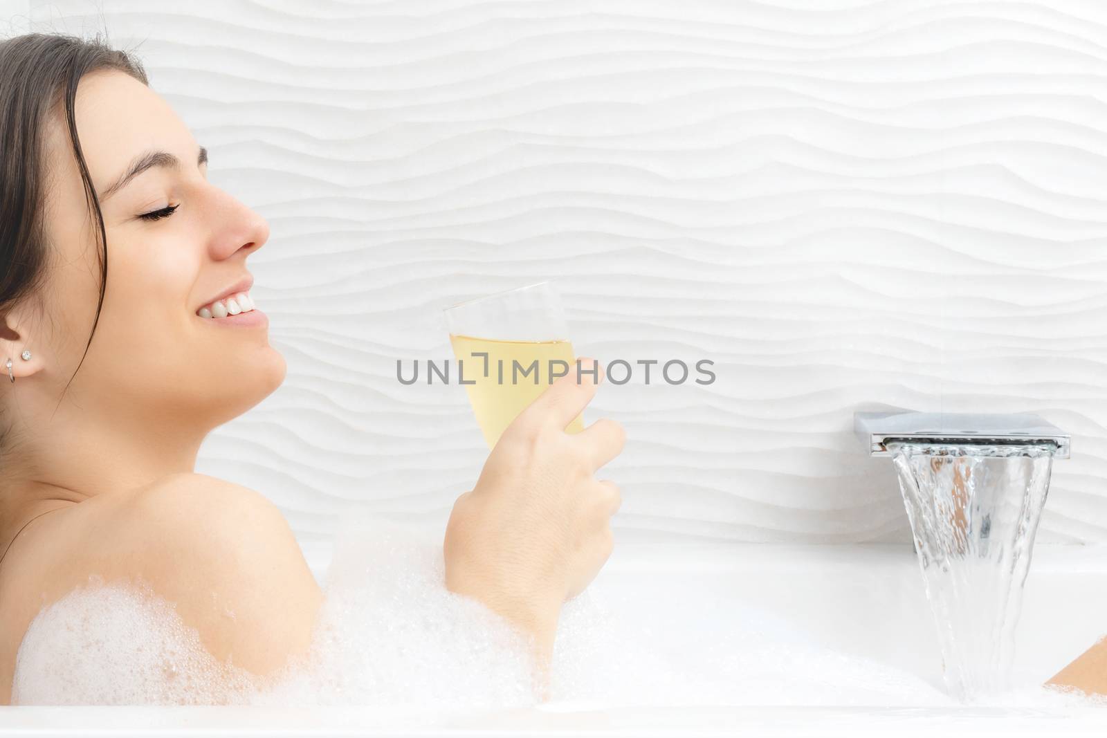 Close up portrait of attractive young woman enjoying champagne in foam bath.