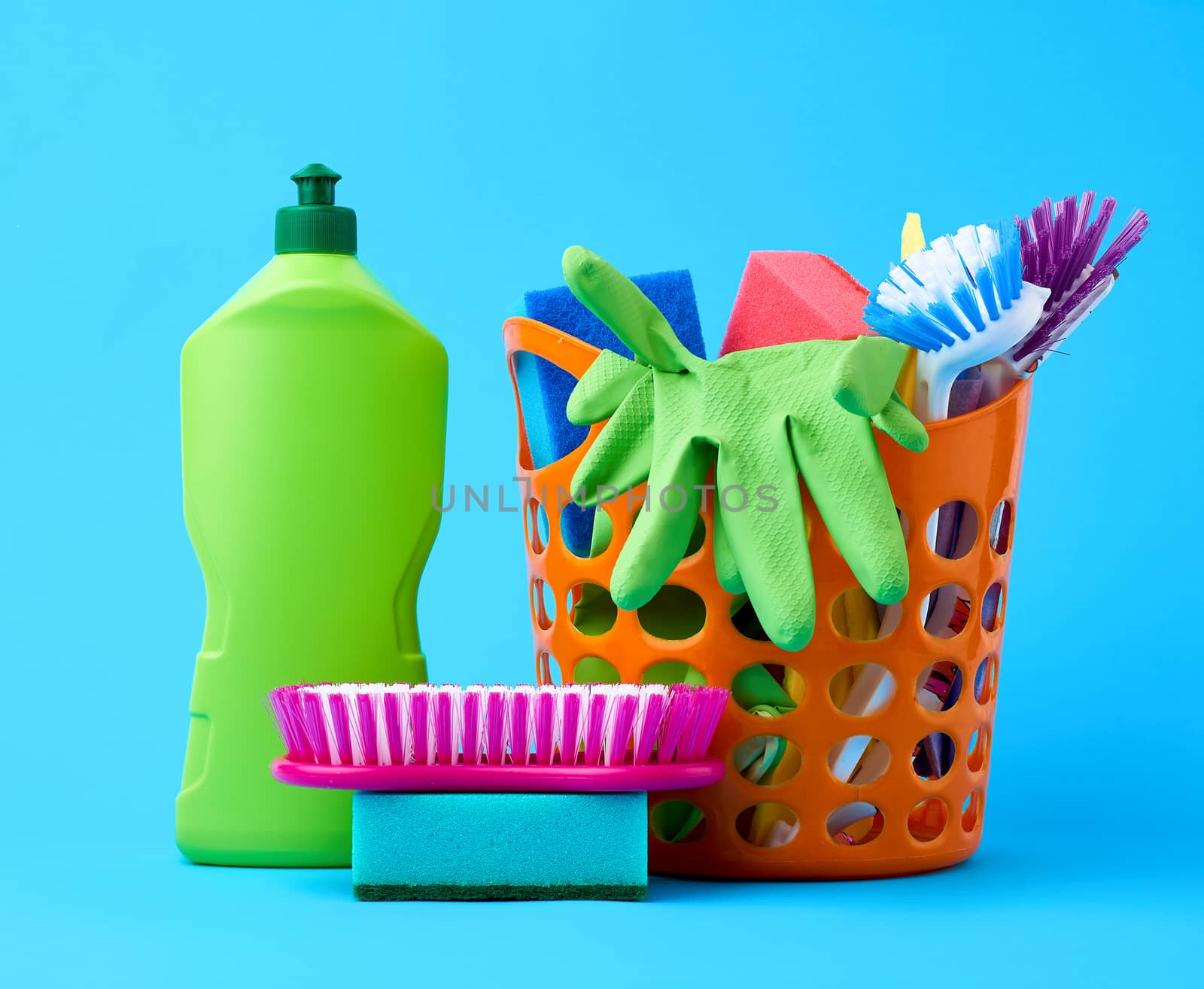 orange basket with washing sponges, rubber protective gloves, brushes and cleaning agent in a green plastic bottle on a blue background, set