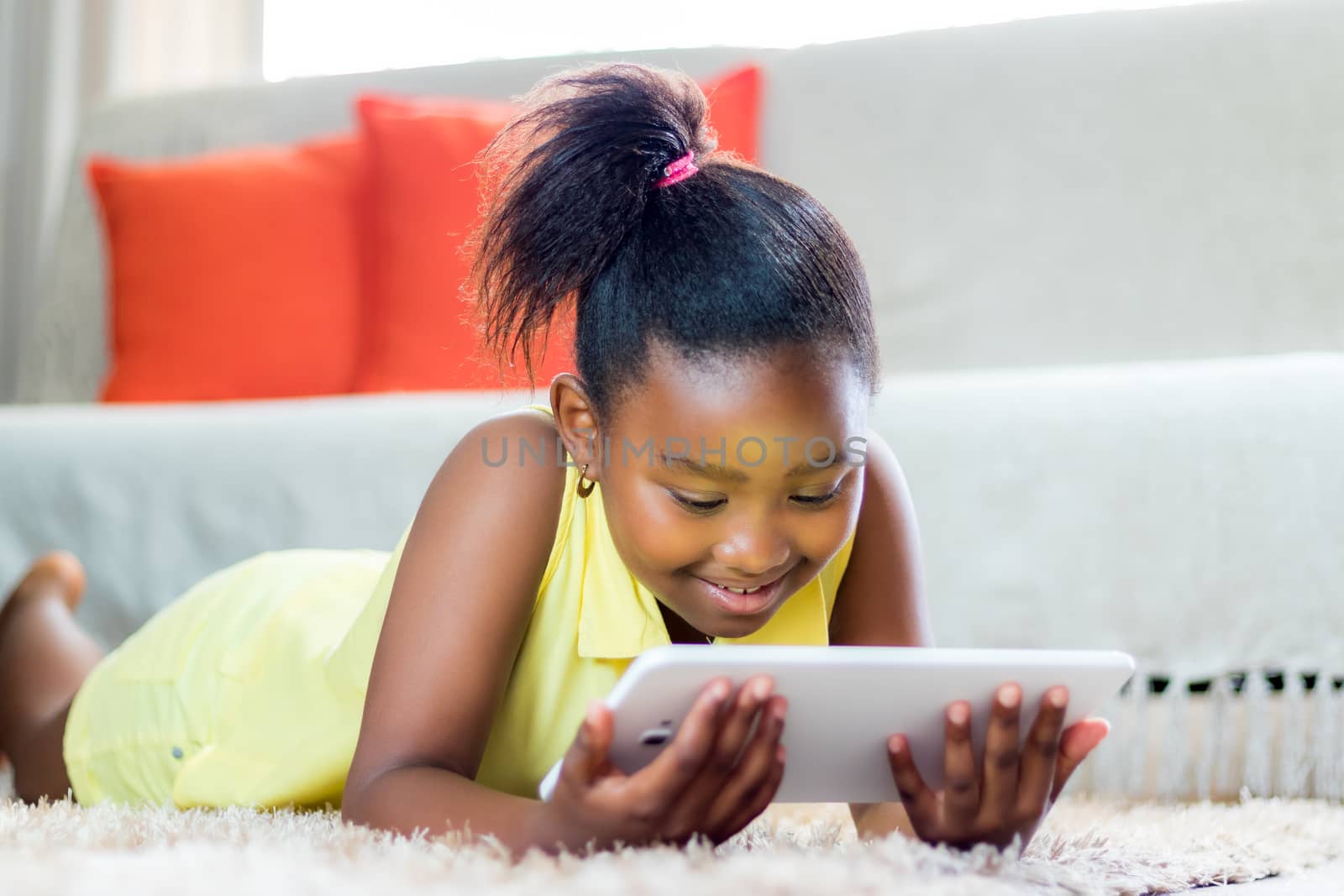 Little african girl playing on tablet in living room. by karelnoppe