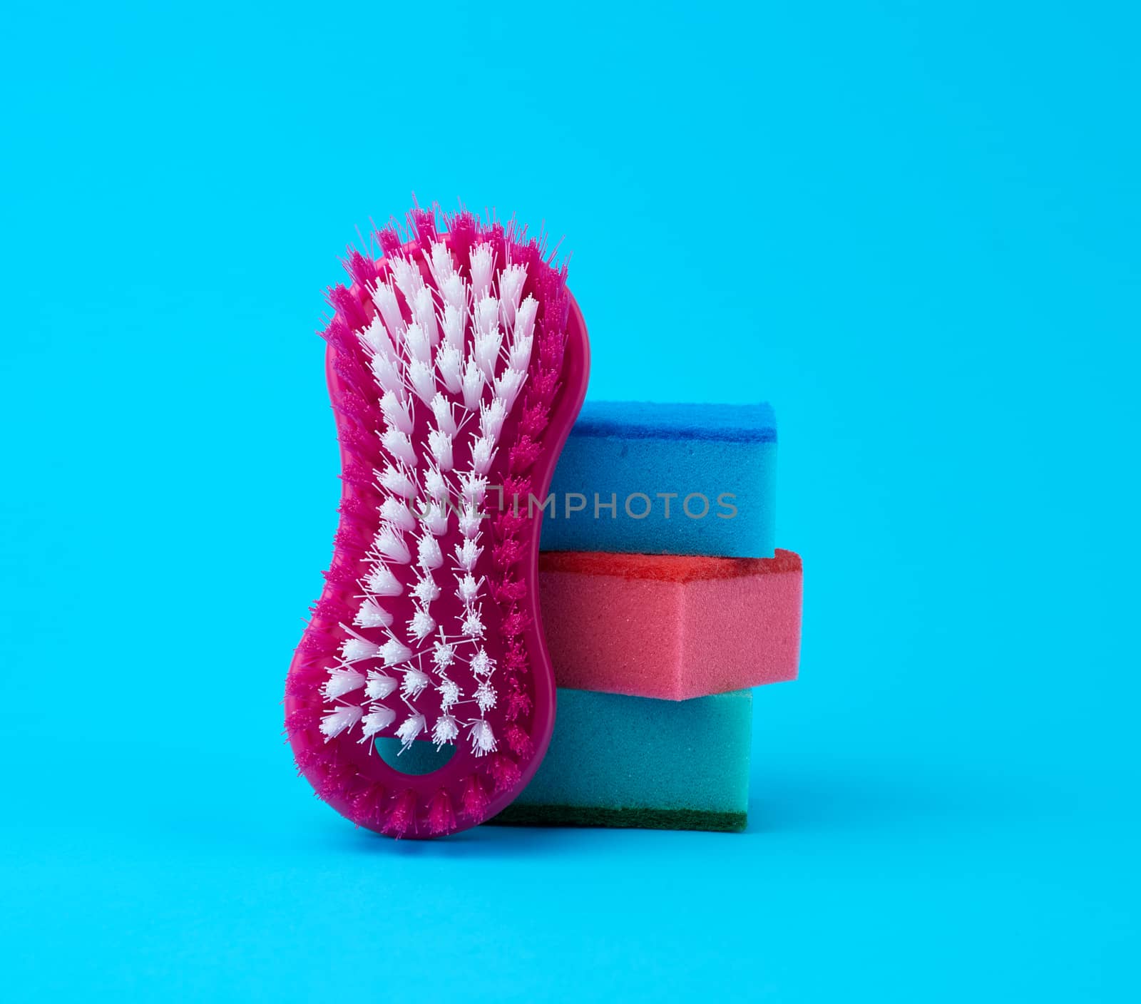 stack of multi-colored kitchen sponges for washing dishes and a red brush on a blue background