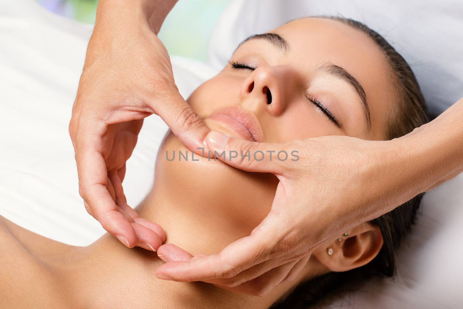 Close up of woman having facial beauty treatment in spa. Therapist applying revitalizing cosmetic product on chin.