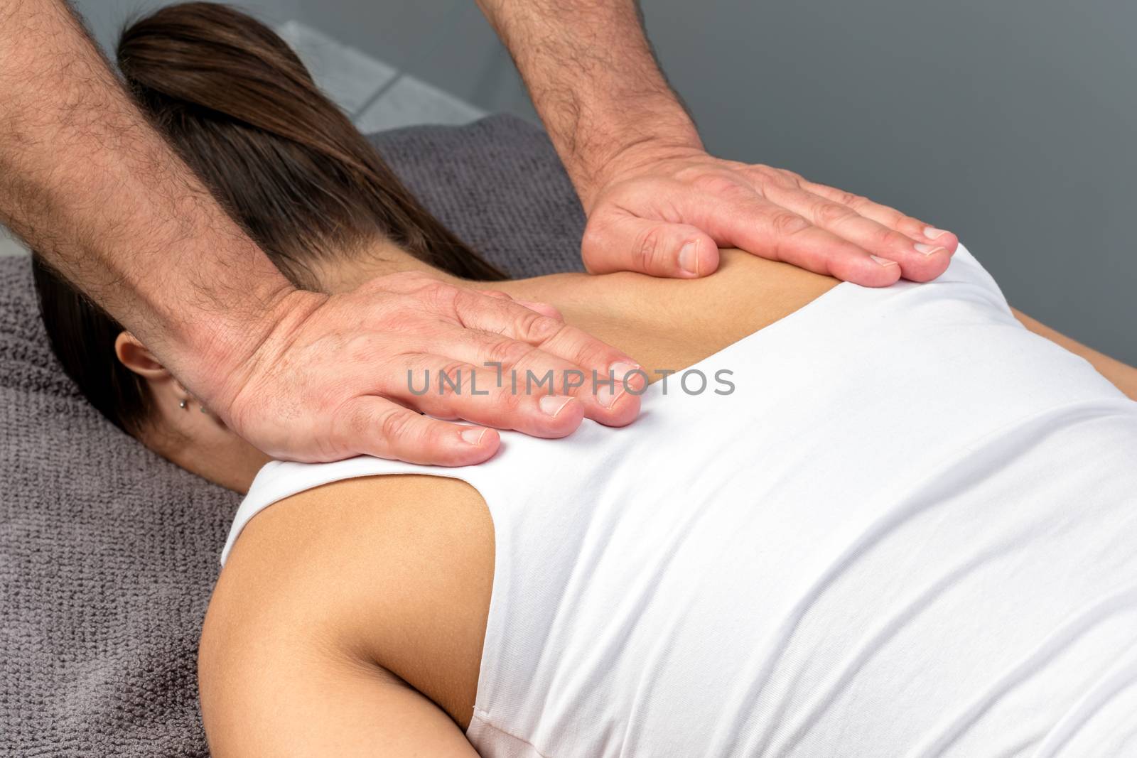 Close up detail of therapist applying pressure with hands on female shoulder.