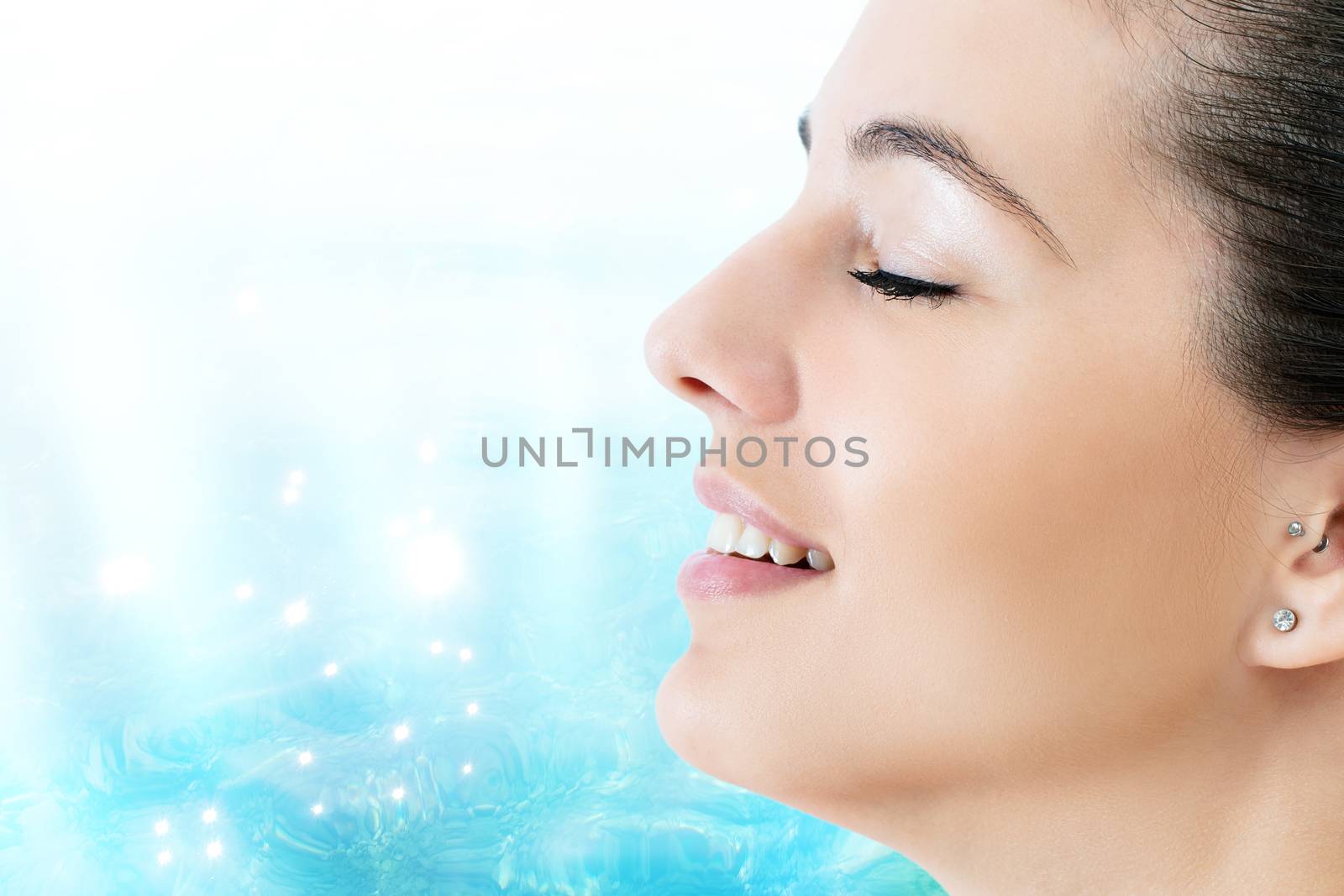 Macro close up side view face shot of young woman with eyes closed.Attractive girl smiling against light blue water background.