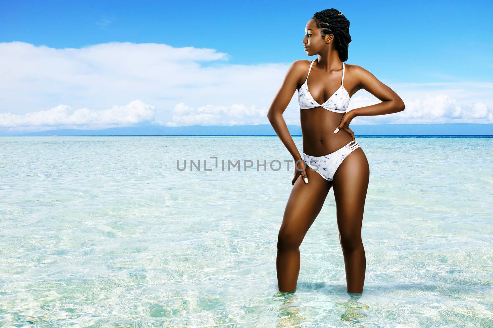 Close up portrait of attractive young african woman wearing bikini.Girl with braided hairstyle standing in shallow water in lagoon. Idyllic sunny holiday landscape.