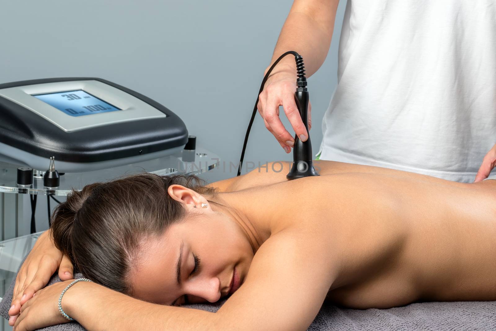 Close up of young woman receiving interferential electrotherapy.Therapist stimulating nerve on spine with apparatus.